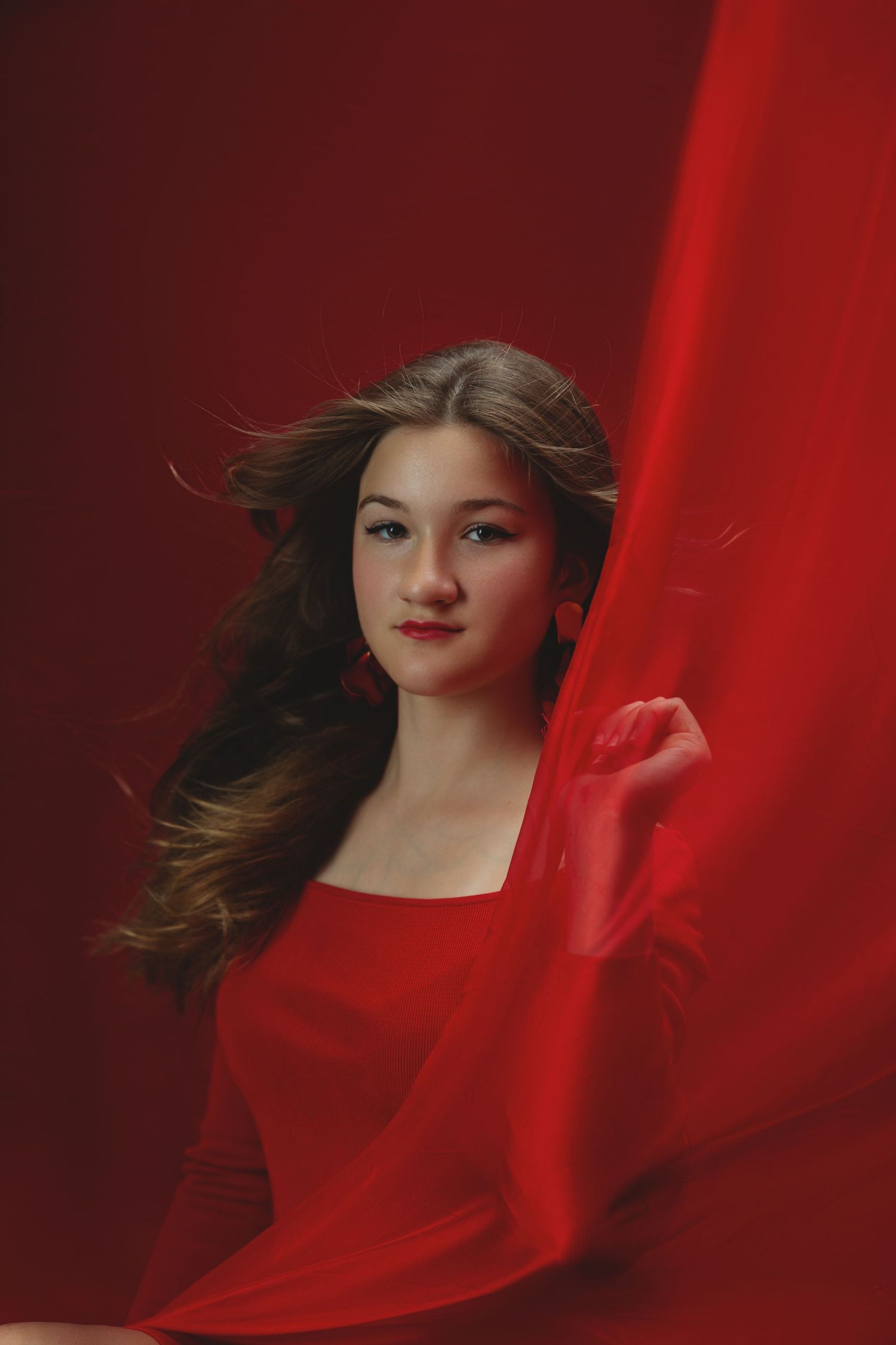 Artistic portrait with flowing red fabric creating dramatic movement and lighting effects.