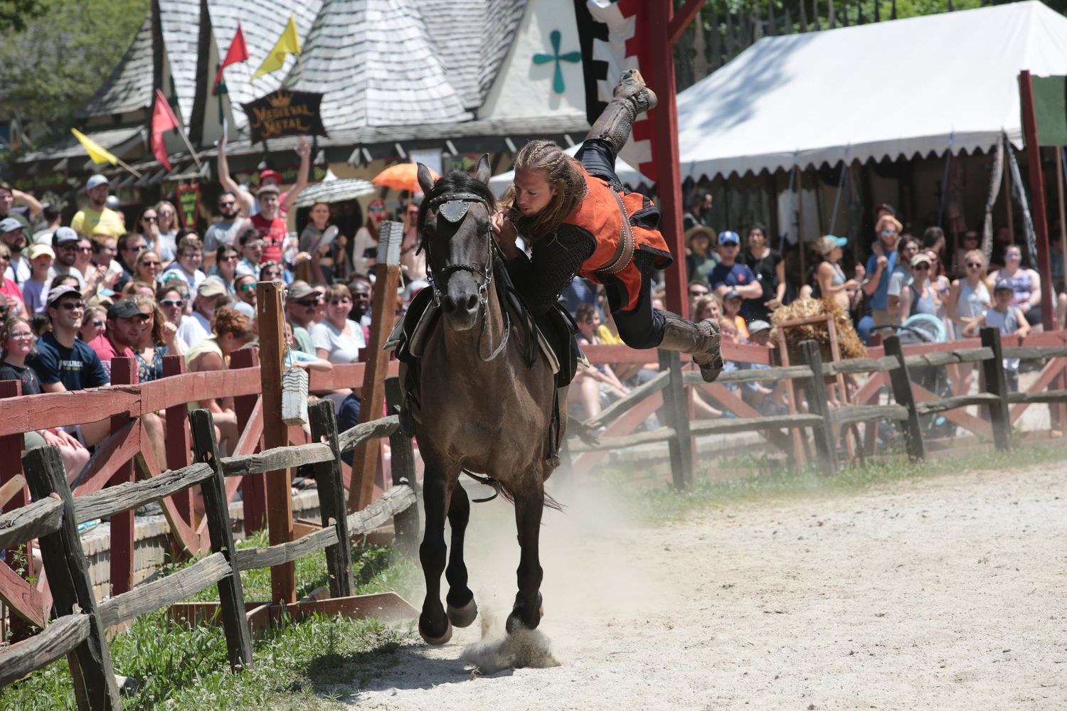Medieval jousting tournament with armored knights on horseback charging at each other in an outdoor arena.