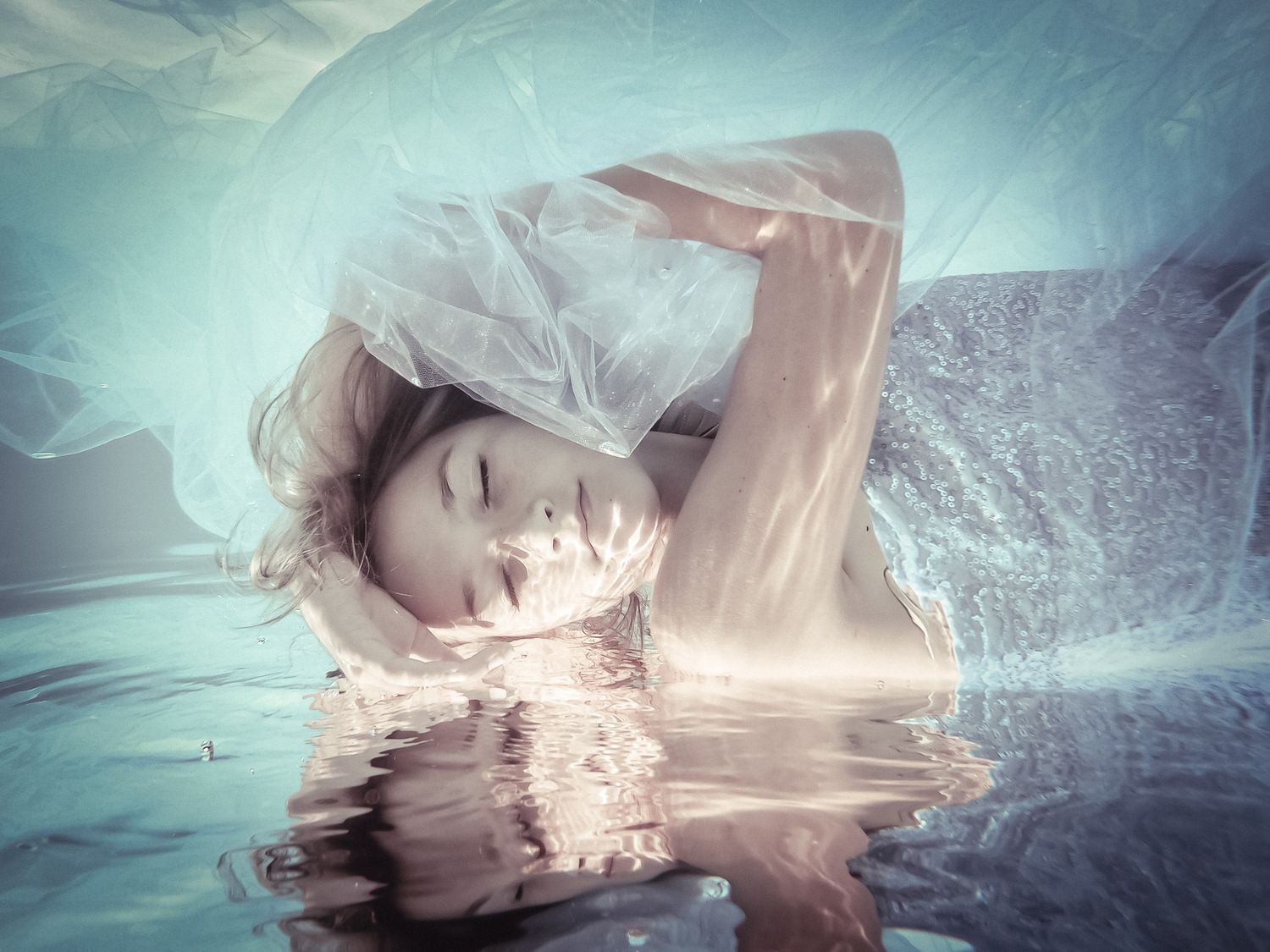 Artistic underwater portrait with ethereal reflections and dreamy aqua tones.