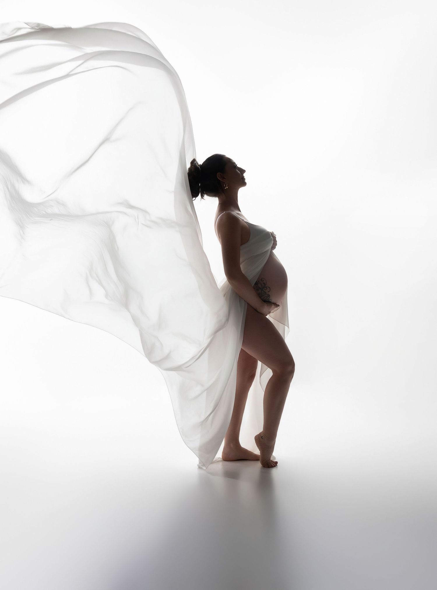 Artistic maternity silhouette series with billowing white fabric in bright studio setting.