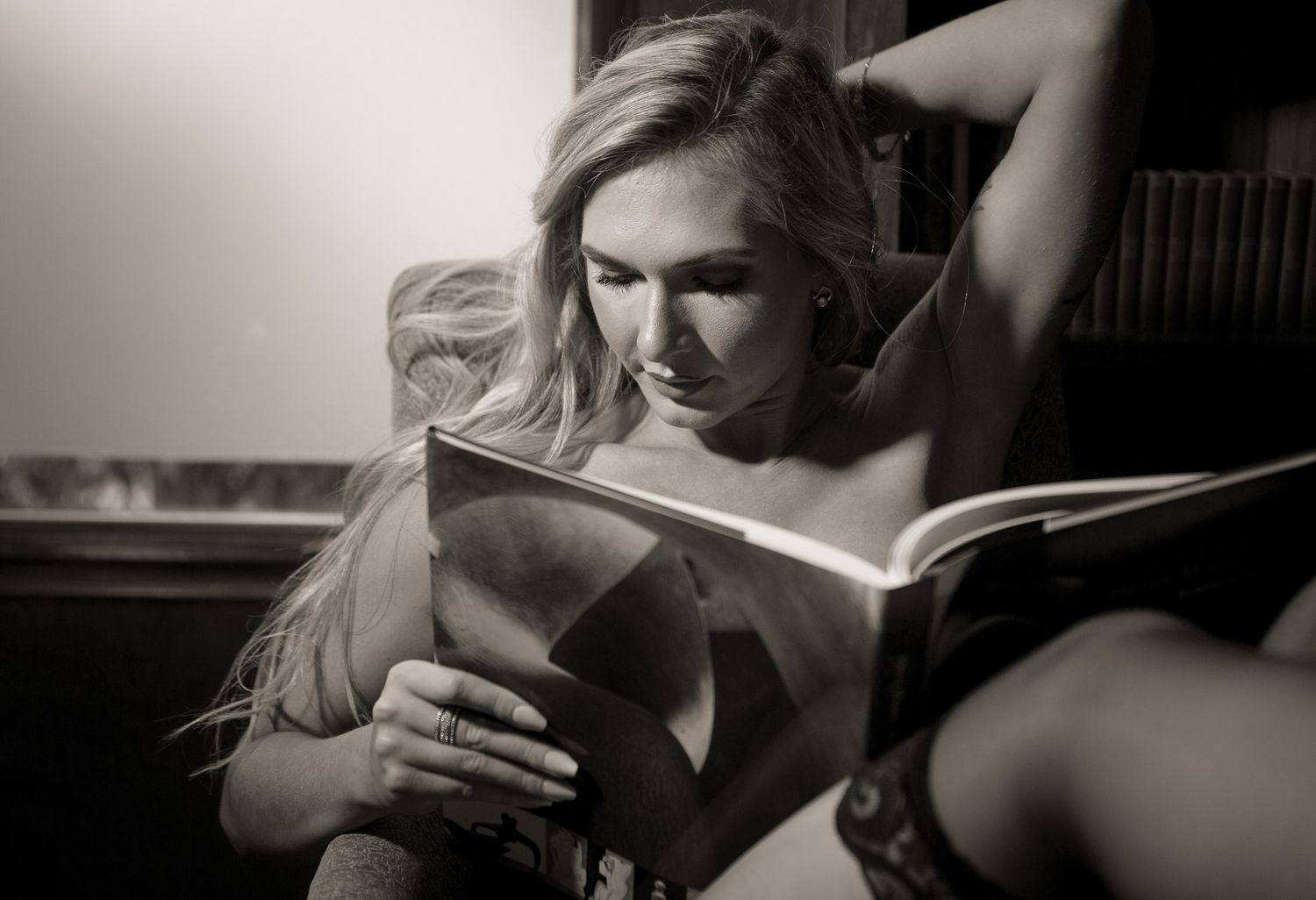 Person relaxes while reading book in moody black and white photograph.