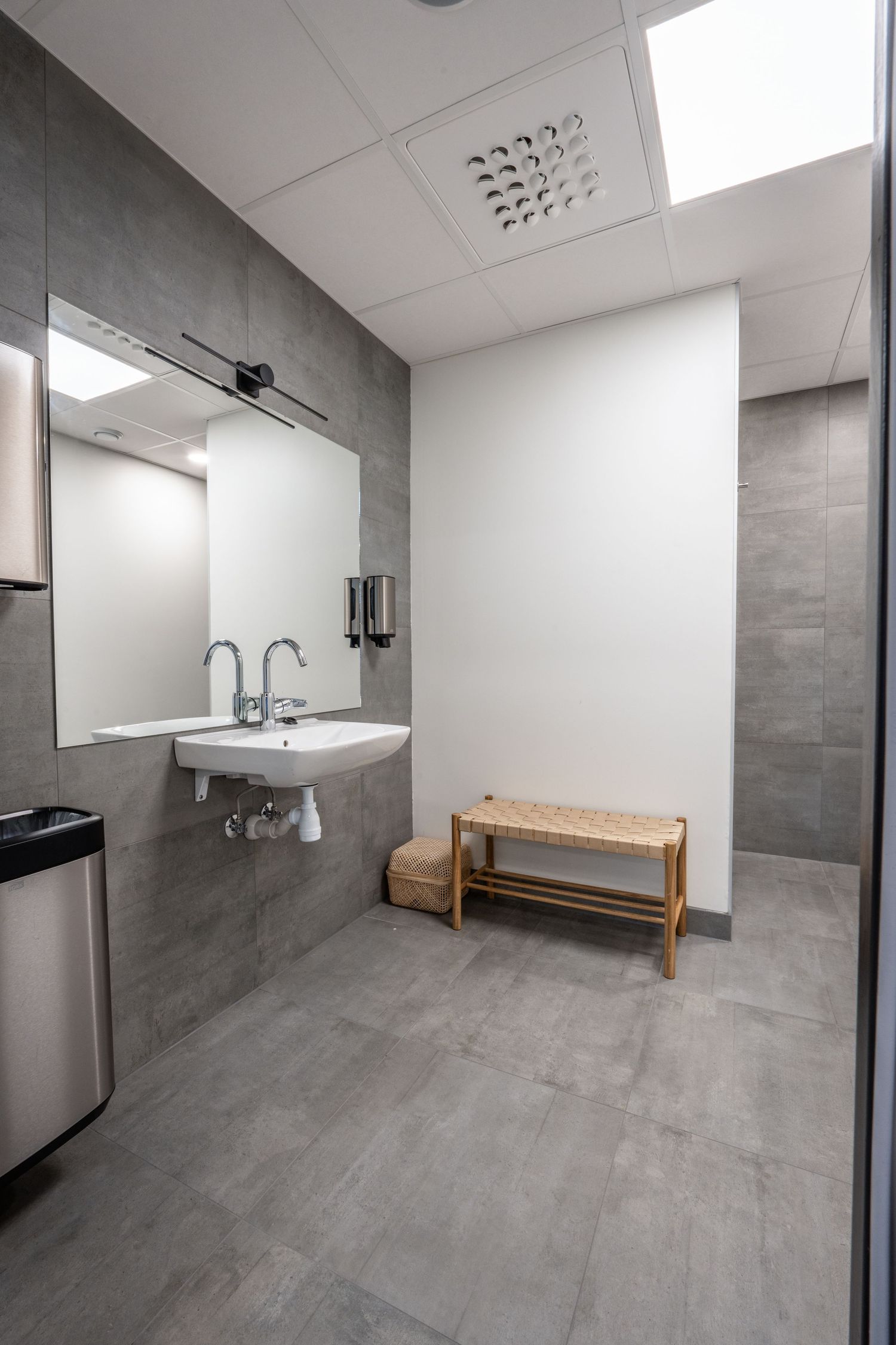Clean modern bathroom with gray tile floors, white sink and wooden bench seating.