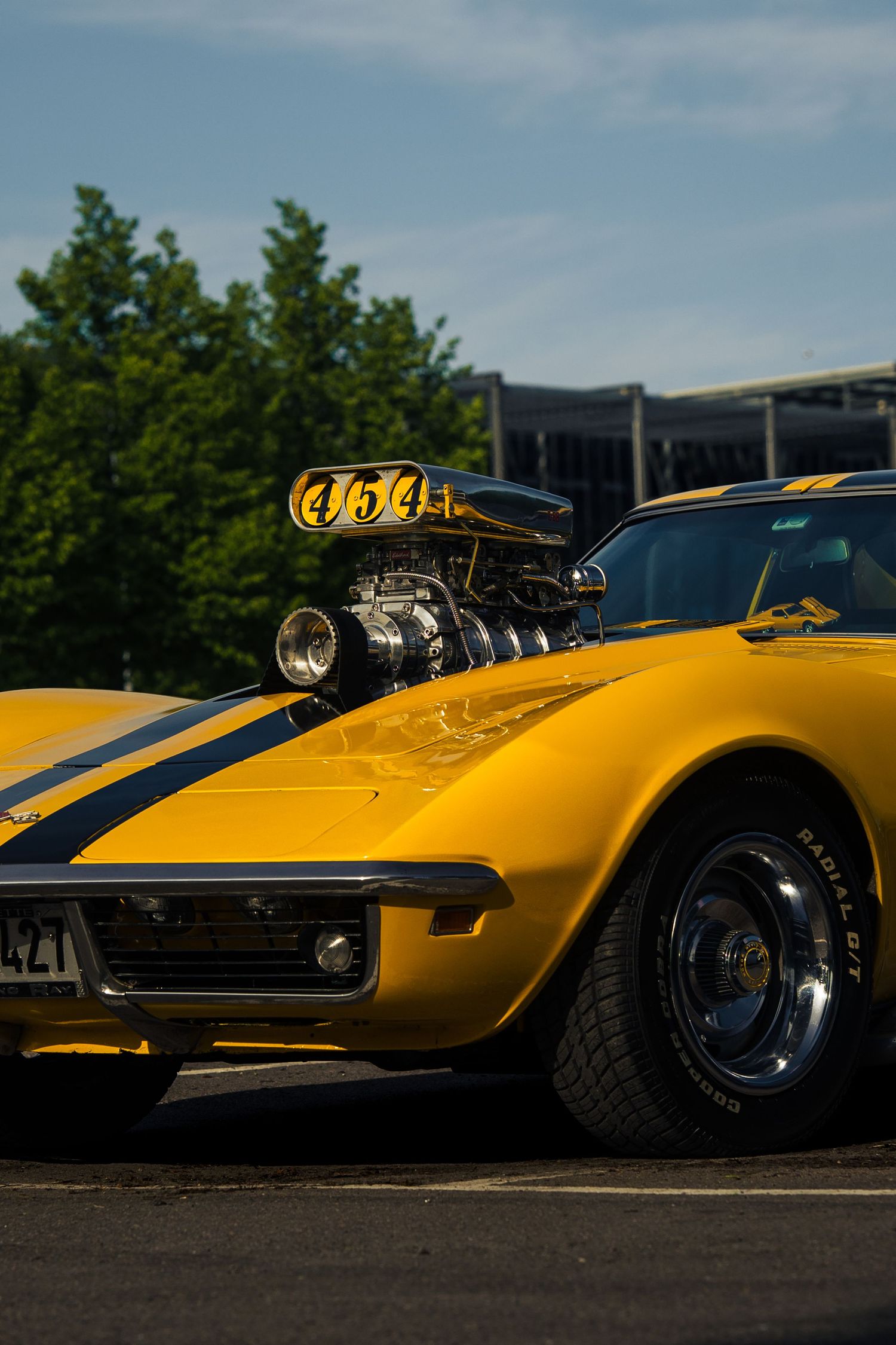 Modified yellow Corvette with exposed supercharger engine and racing stripes.