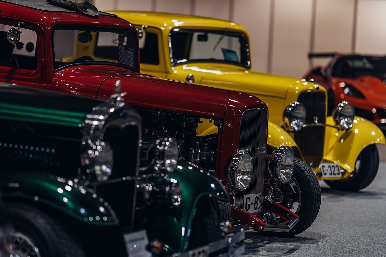 Classic vintage cars in green, red, and yellow colors lined up at an indoor auto show.