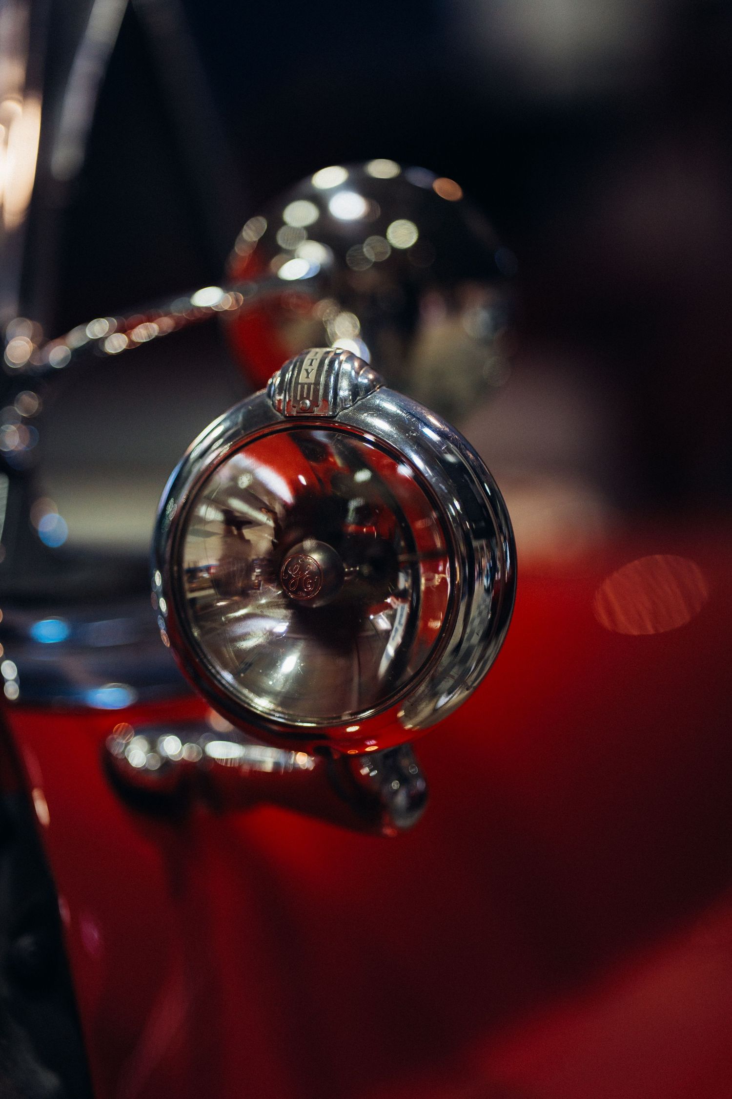 Vintage chrome automobile headlight with red reflections and bokeh lighting effects.