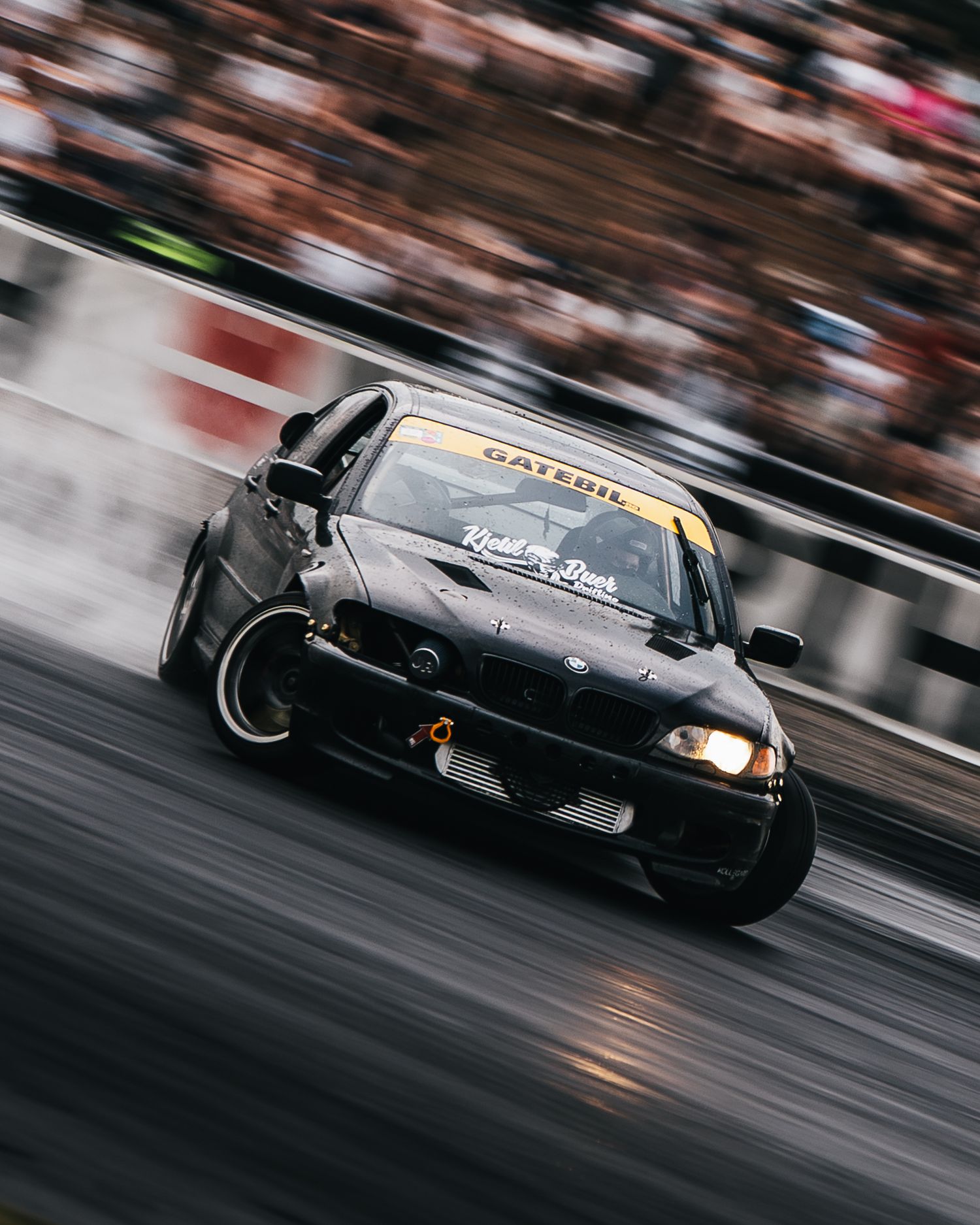 Black sports car drifting on a race track with motion blur and smoke from tires.