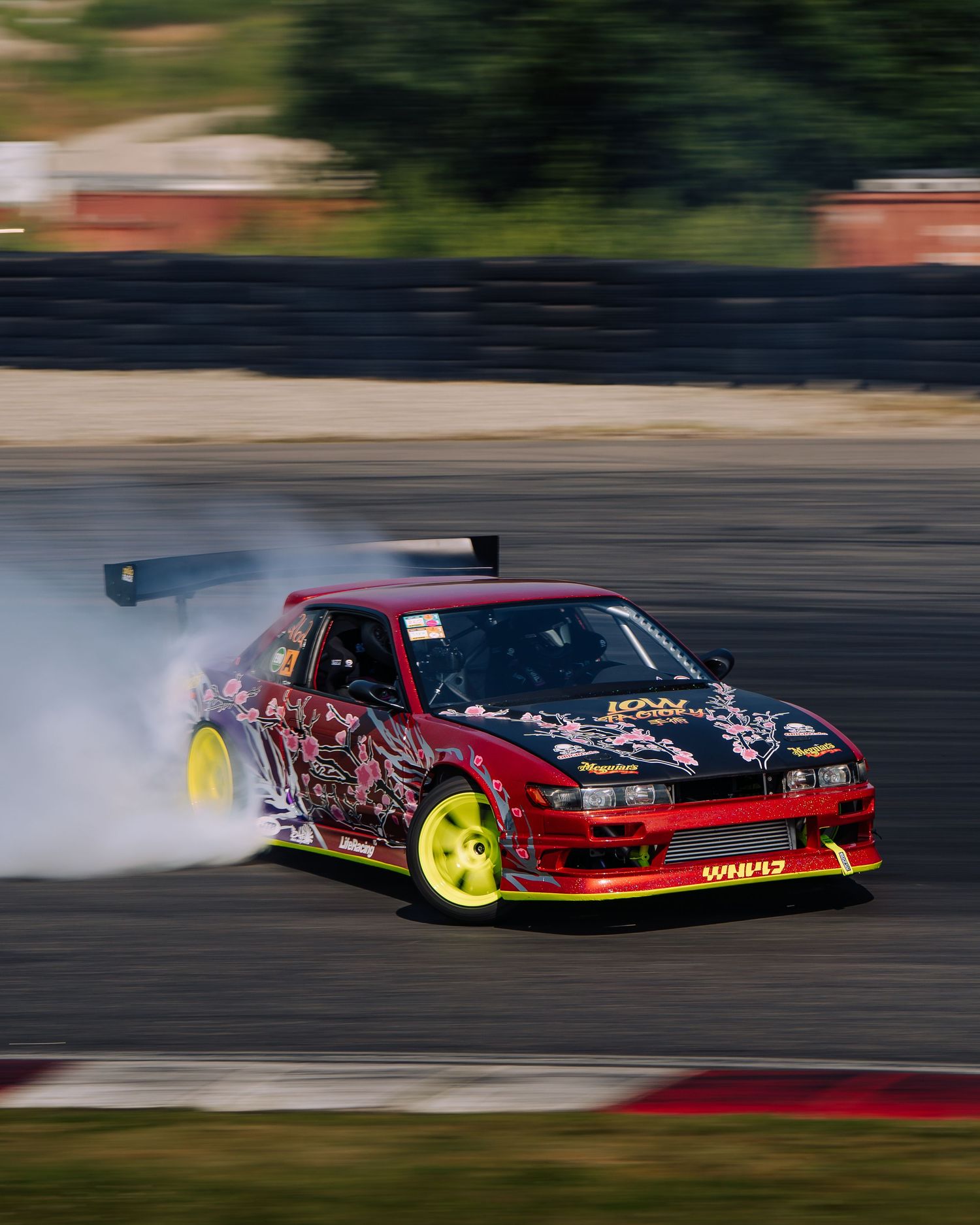 A red drift car slides sideways on a race track creating smoke from the tires during a drifting competition.