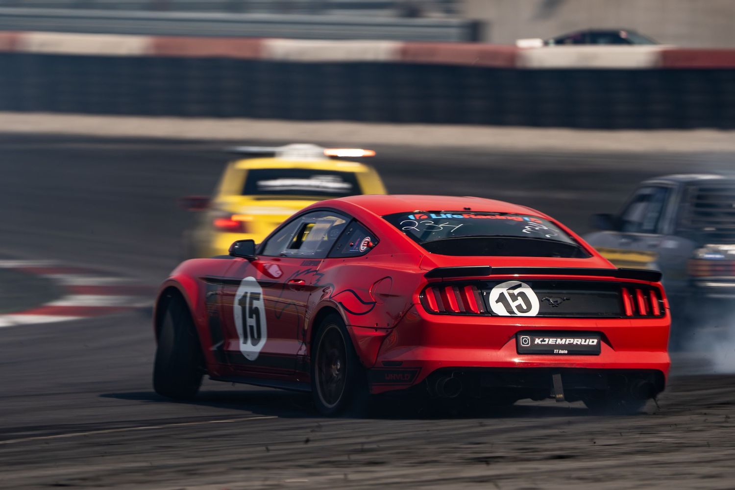 Red sports cars drift around a race track creating smoke trails during a competitive drifting event.