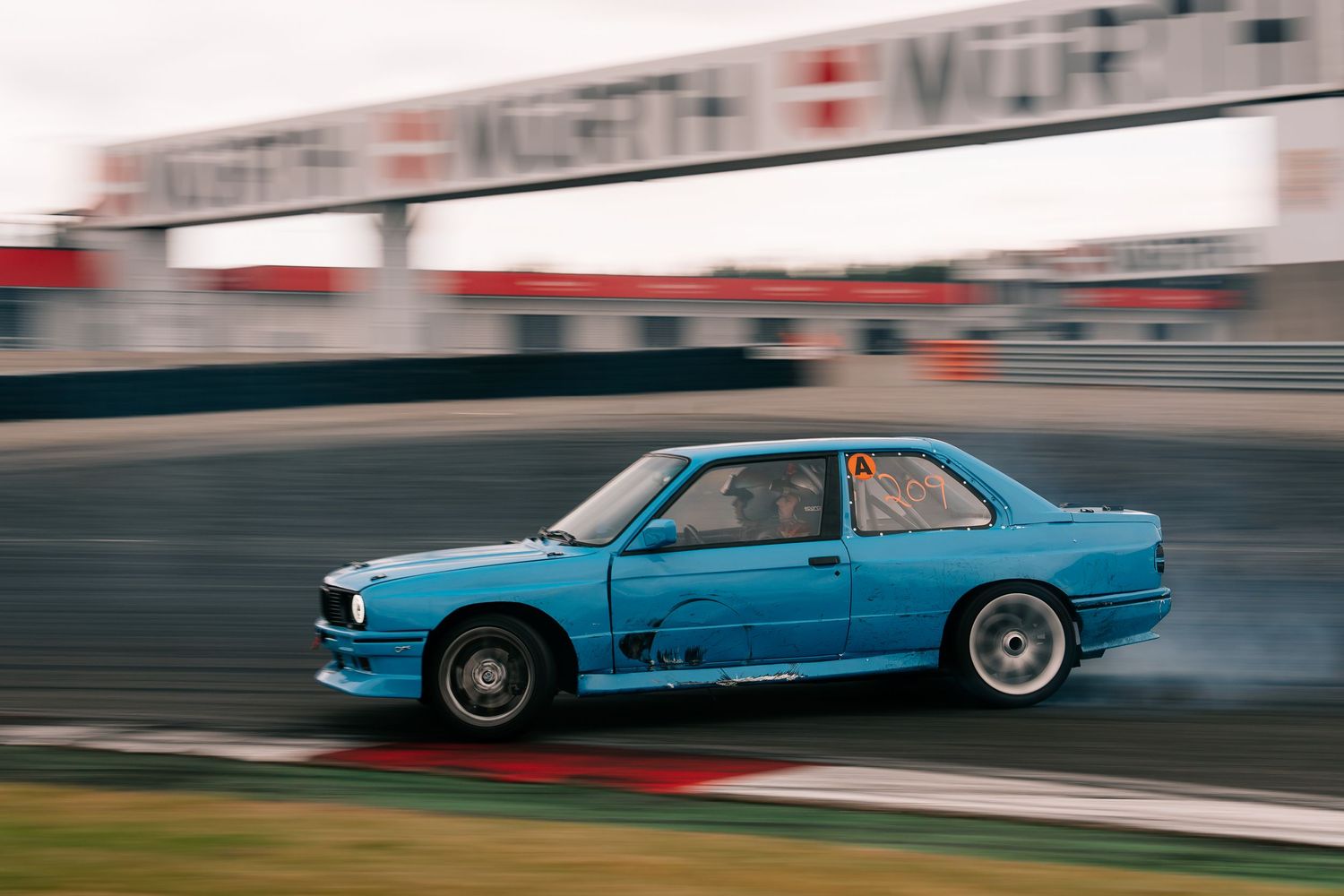 A light blue vintage car races around a track with motion blur, showcasing its classic styling and performance.