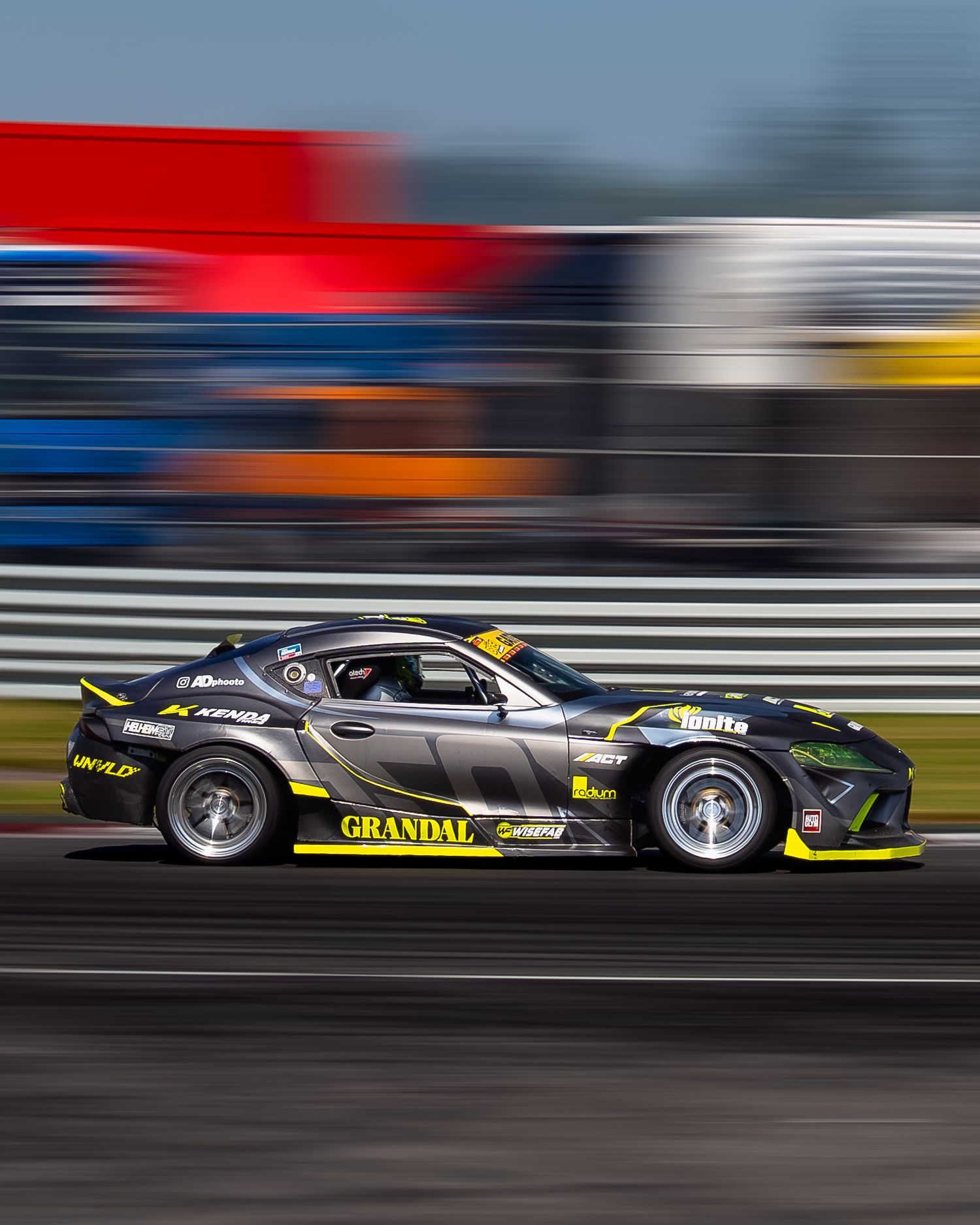Racing car in motion on track with motion blur effect creating dynamic speed impression during competition.