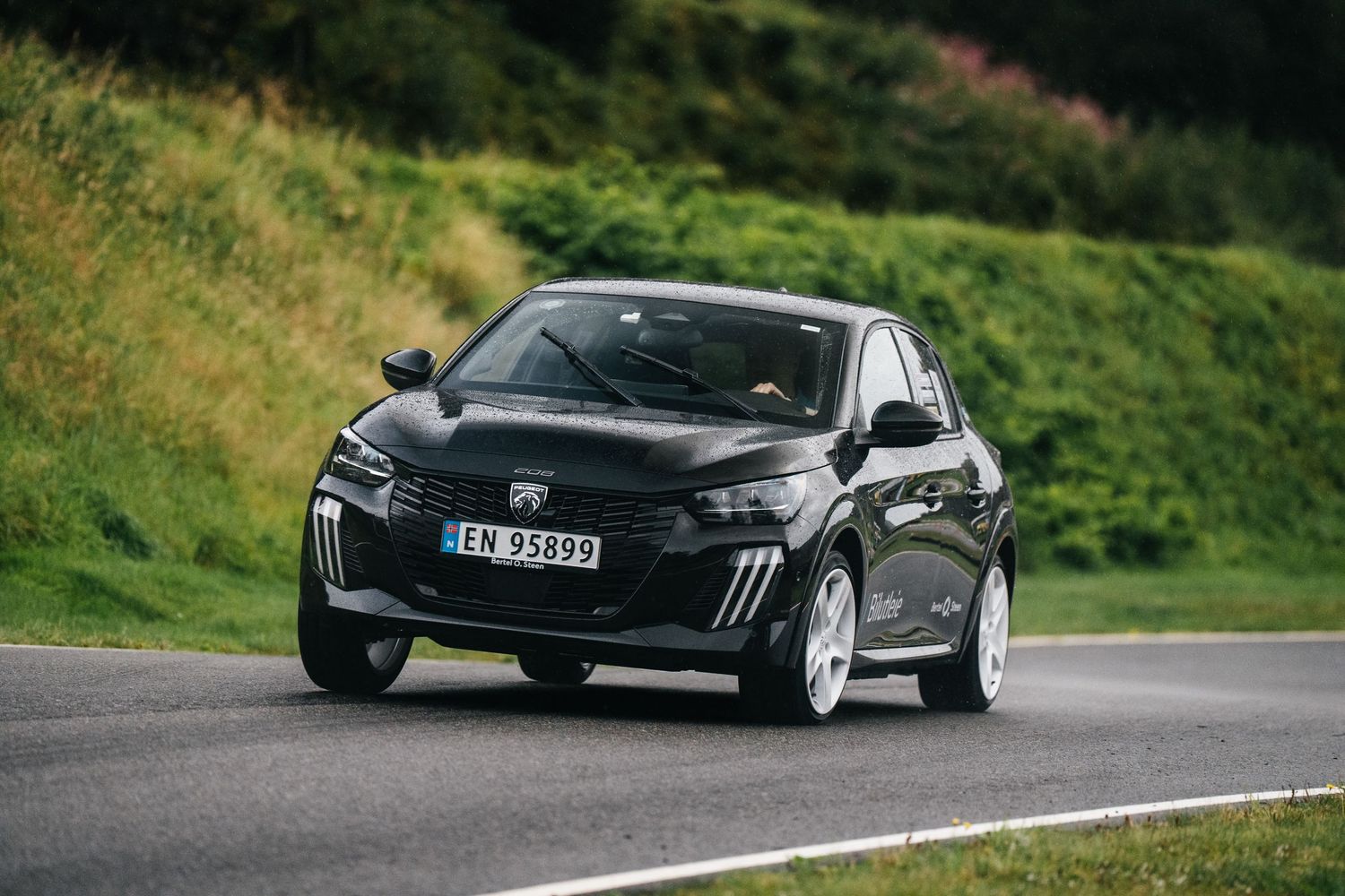 Black sports car driving on a winding mountain road with lush green scenery in the background.