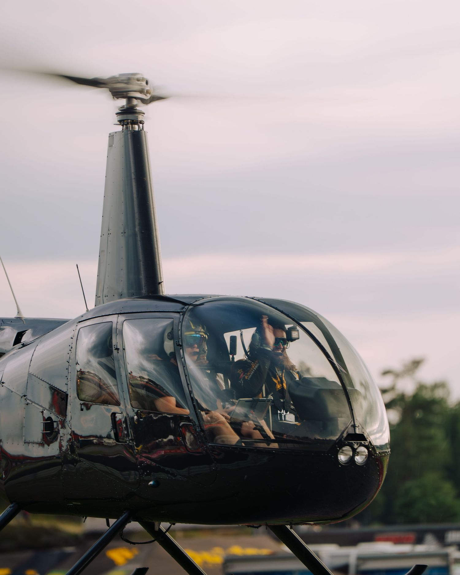 A sleek black Robinson R44 helicopter parked on the tarmac during sunset with a clear view of its cockpit.