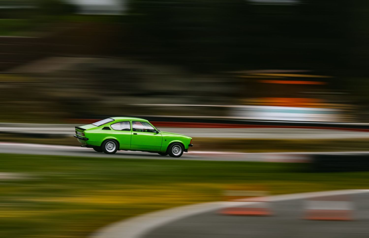A bright green vintage muscle car speeds along a winding road, creating motion blur against the forested background.
