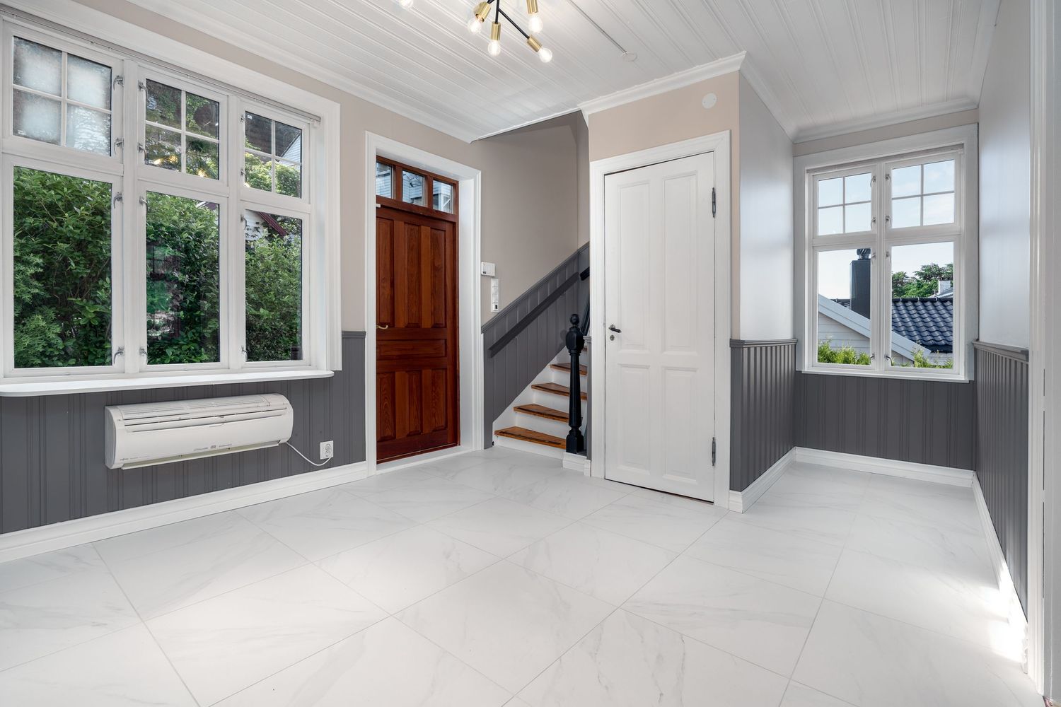 Bright entryway with white trim, wooden front door, and grey wainscoting.