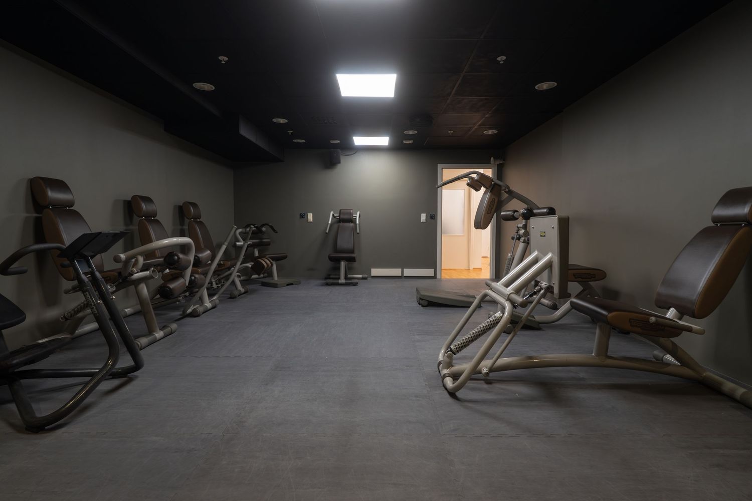 Dimly lit workout area with various exercise machines and equipment on dark flooring.