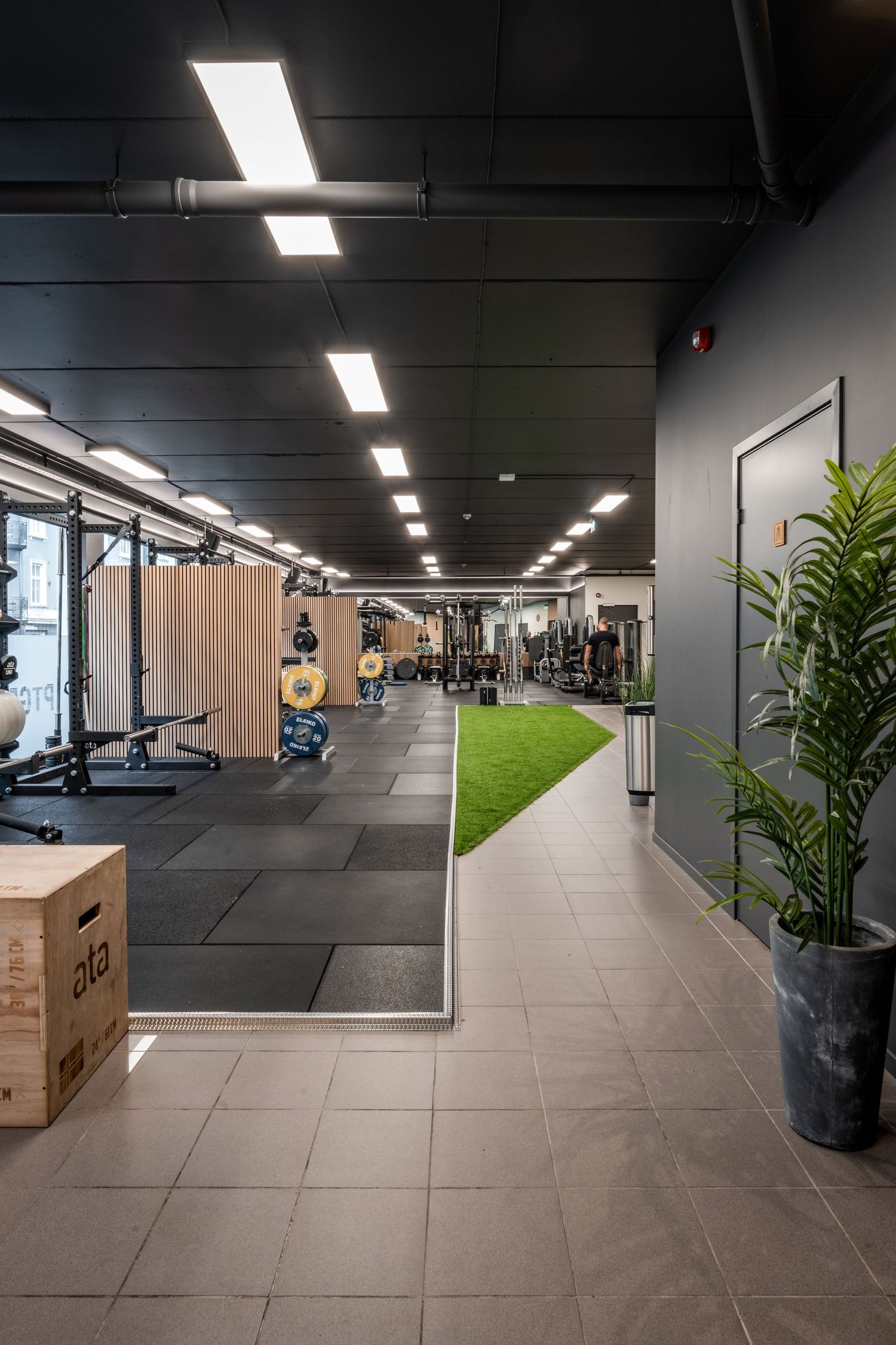 Modern gym interior featuring rubber flooring, wood paneling and an artificial turf strip running through the space.