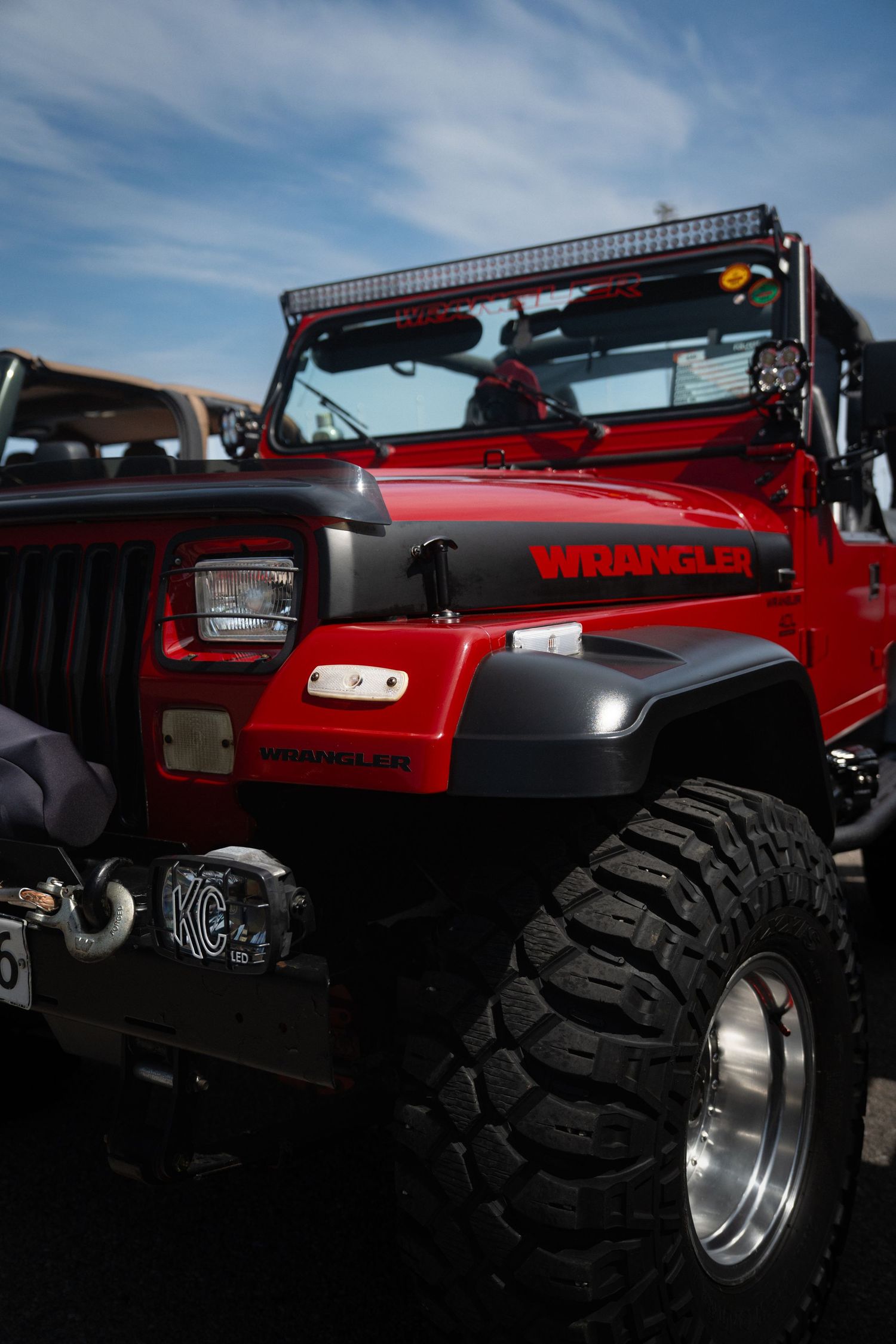 Red Jeep Wrangler with custom off-road modifications and LED light bar photographed at dusk.