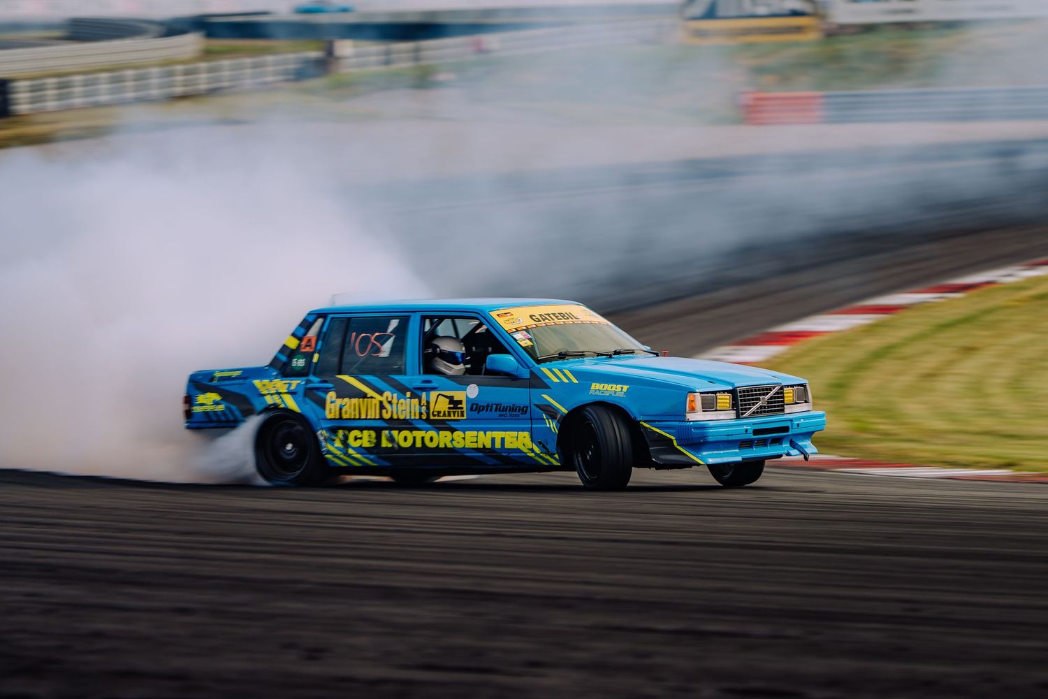 Blue Volvo drift car creating smoke while drifting on a racetrack during competition.