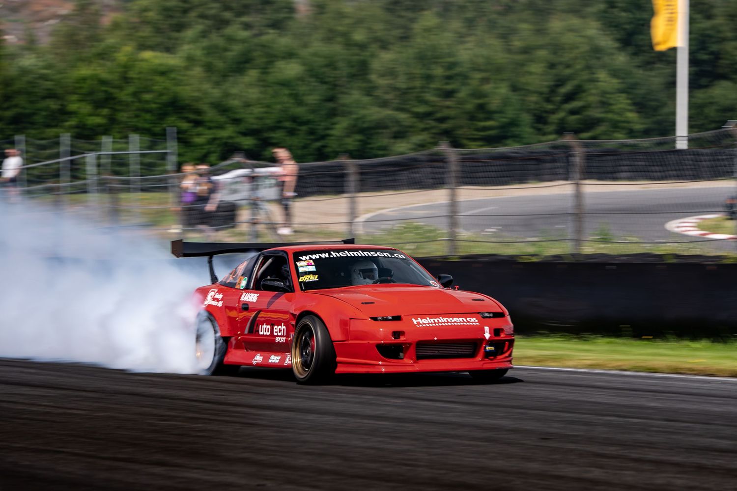 Red sports car drifting on racetrack with smoke trailing behind during competitive motorsport event.