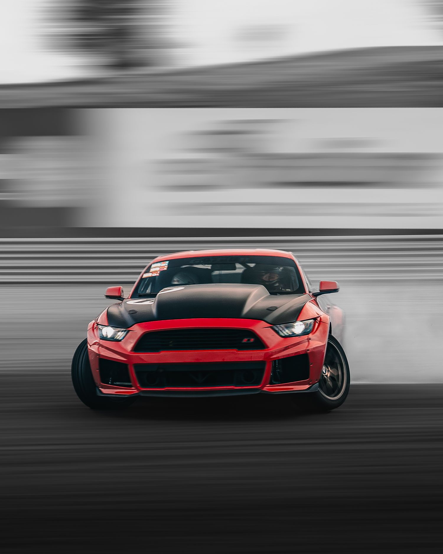 A red sports car with black accents drifting on a track with motion blur effects in monochromatic background.