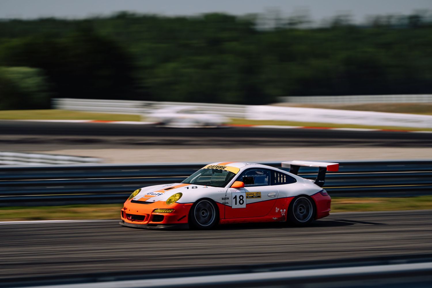 Race cars speed around a track during a motorsport competition on a sunny day.