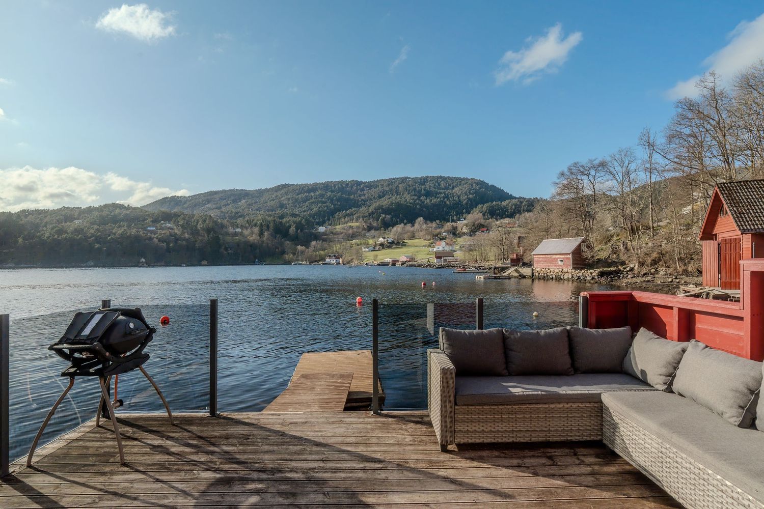 Waterfront deck with outdoor furniture and BBQ grill overlooking scenic Norwegian fjord landscape.