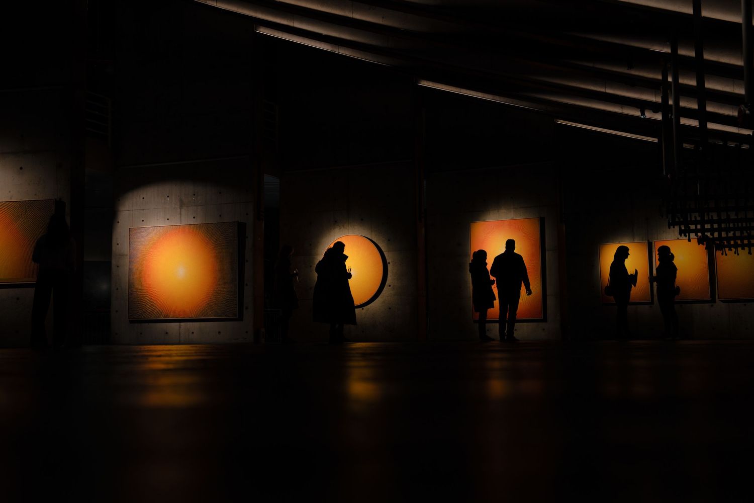 Dramatic silhouetted figures against illuminated panels in an art gallery or museum space.