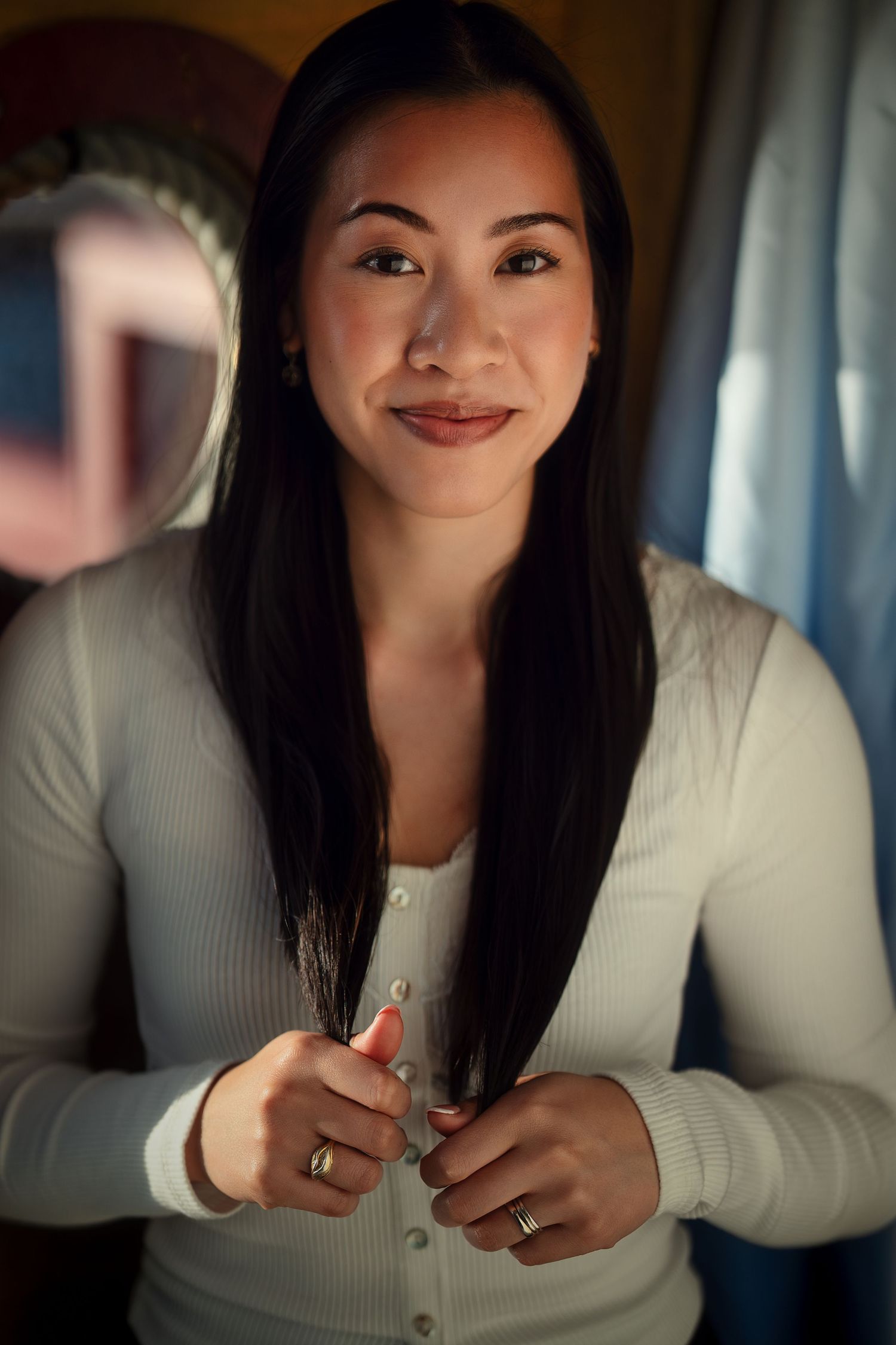 Indoor portrait of woman in white cardigan holding long dark hair.