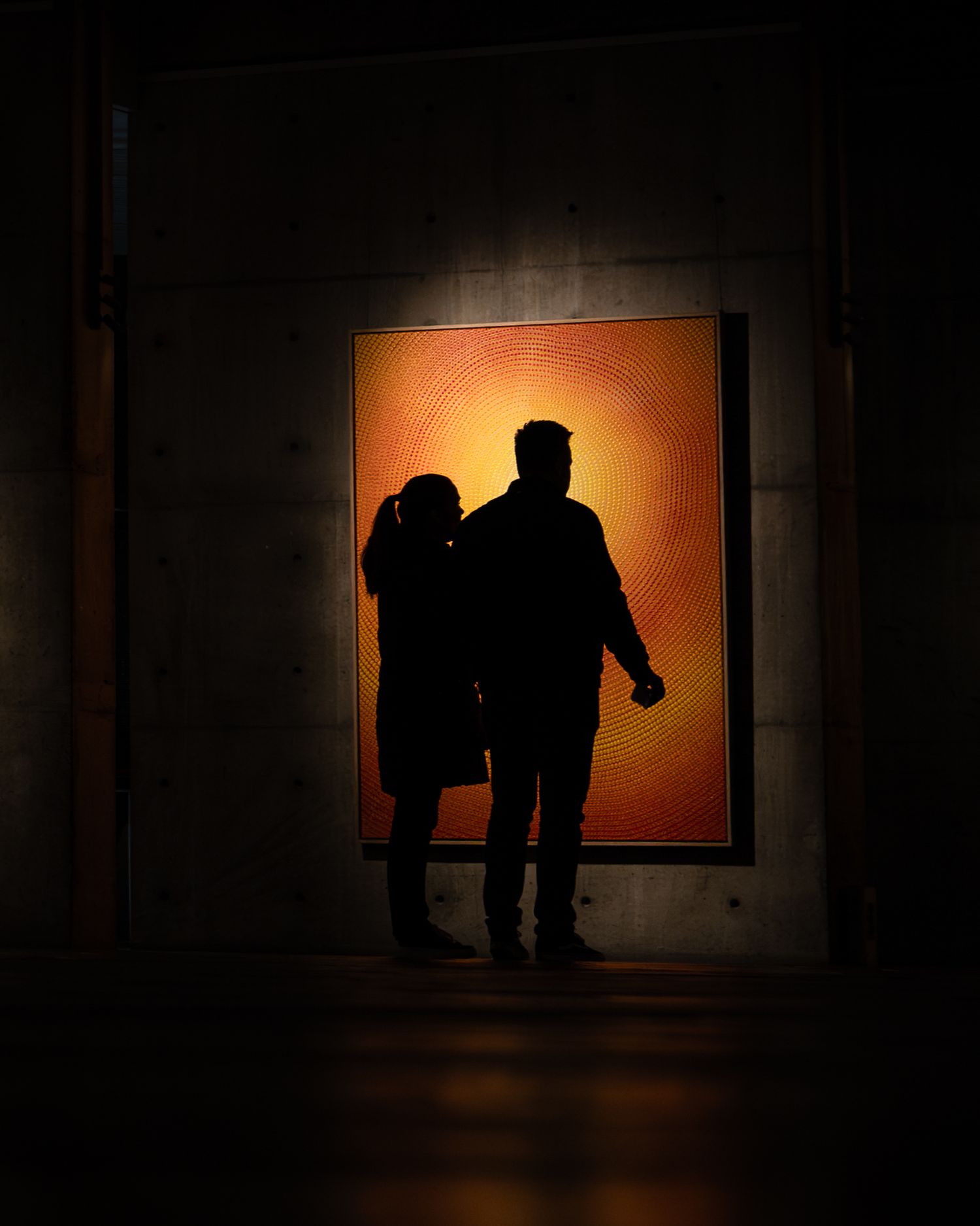 Silhouetted figures against backlit orange wall panel in dark corridor.