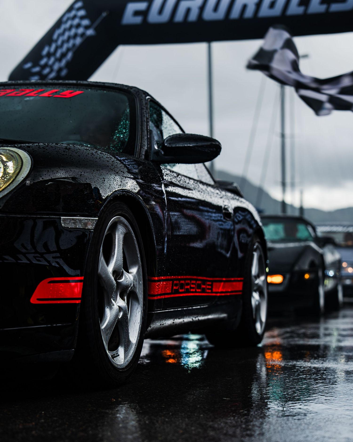Black Porsche with red racing stripe photographed at rainy EuroRally event.