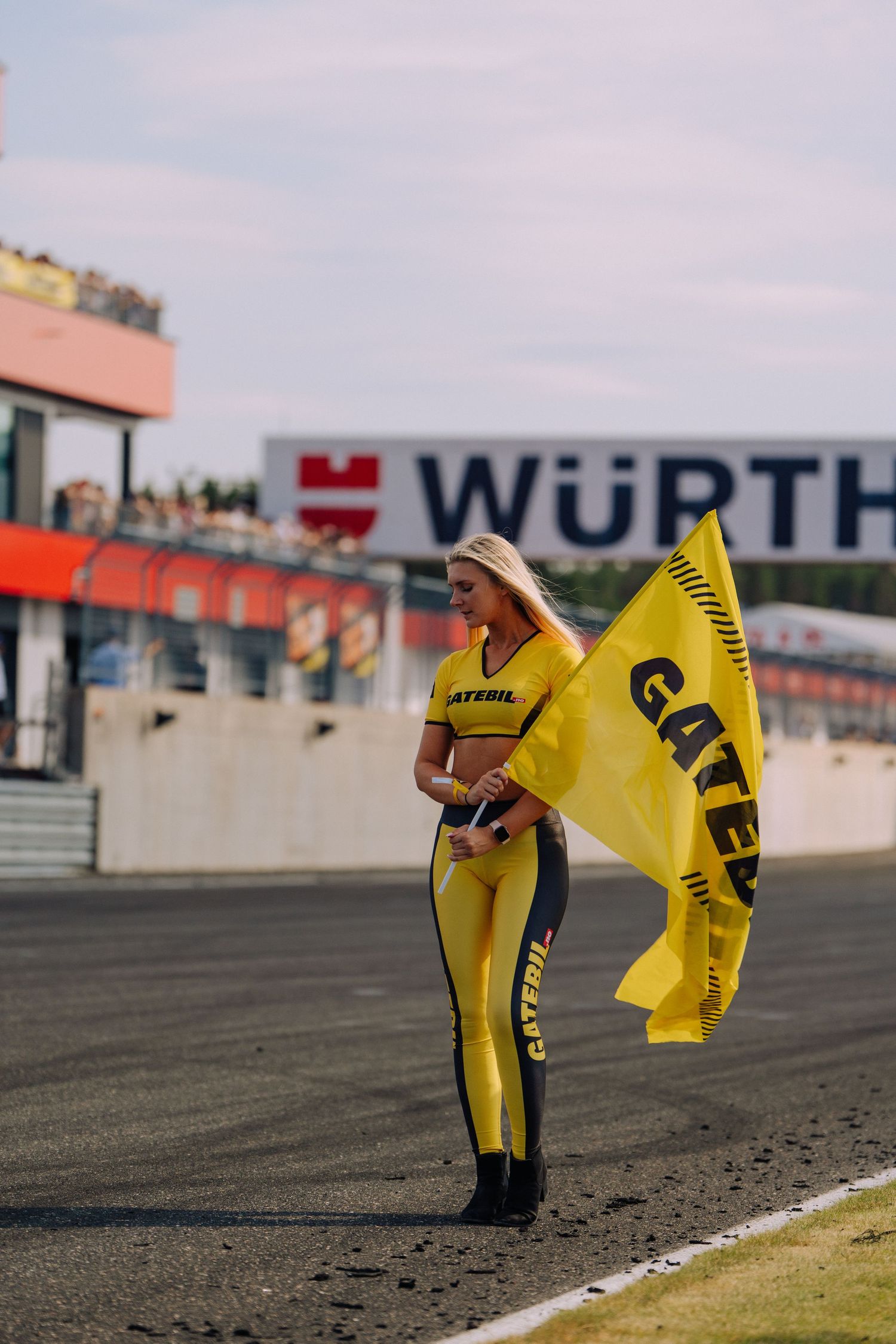 A race grid girl in yellow and black racing suit holding a flag at Wurth racing circuit.