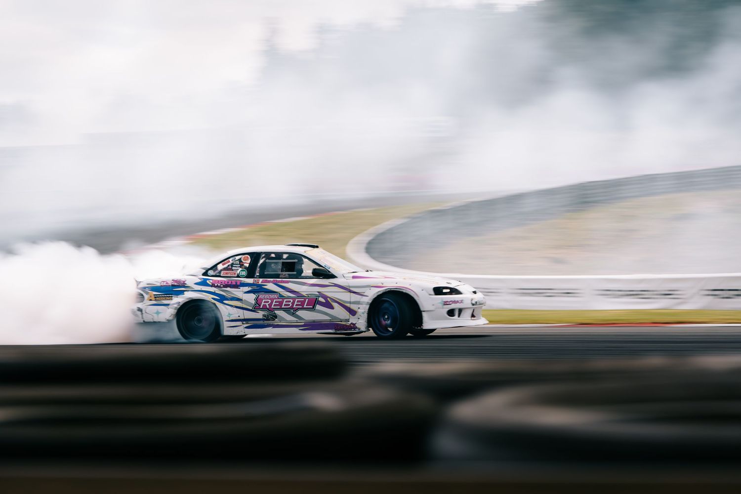 A high-performance drift car creates clouds of smoke while racing around a track during a motorsport competition.