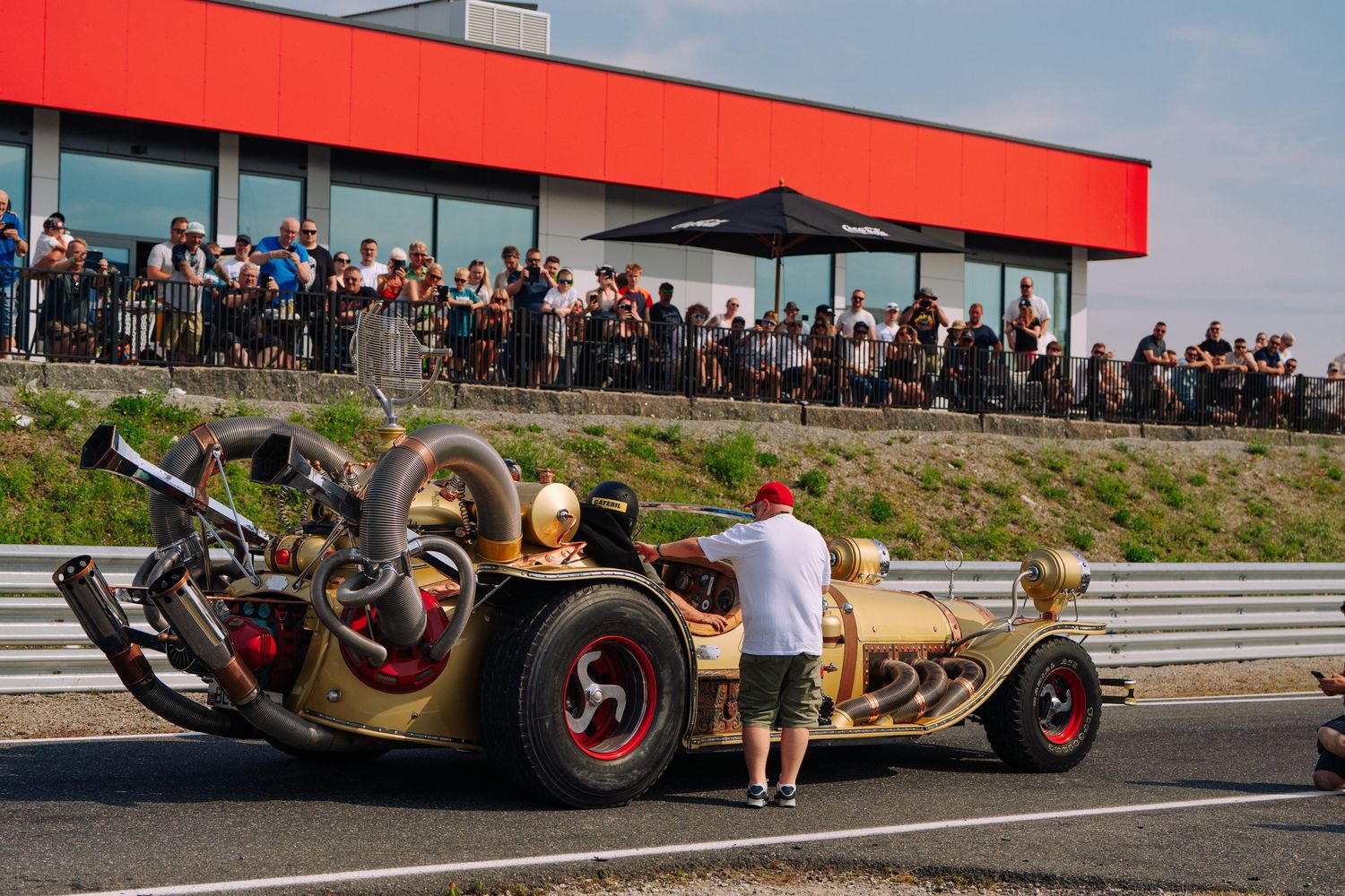 A race car flips upside down during a dramatic crash sequence on a racetrack with spectators watching from the sidelines.