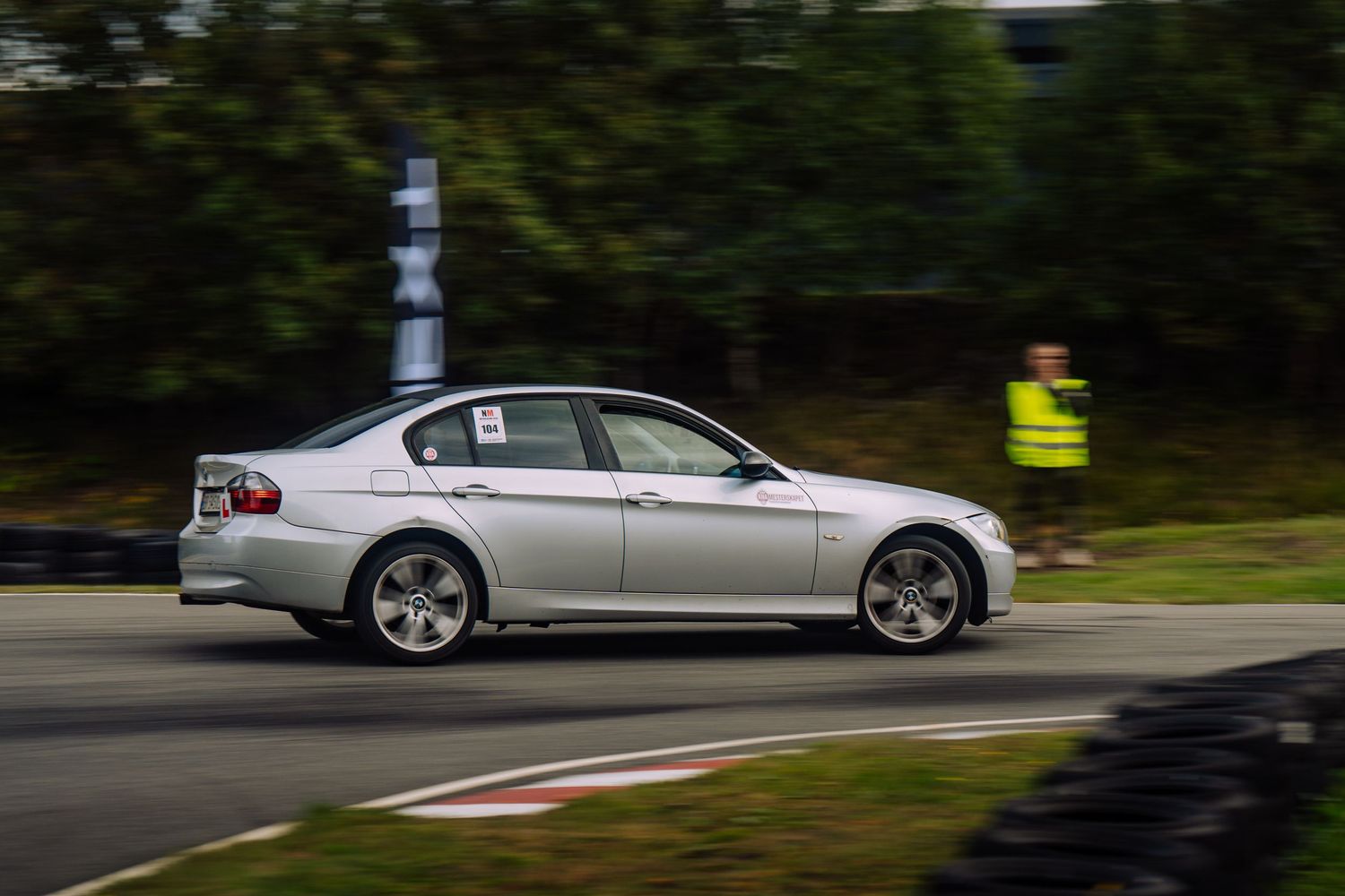A silver BMW 5 series sedan driving on a winding road through a wooded area.