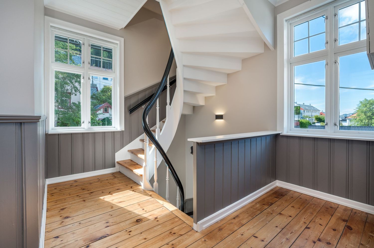 Contemporary living space with spiral staircase, white paneled walls, and light wooden flooring.