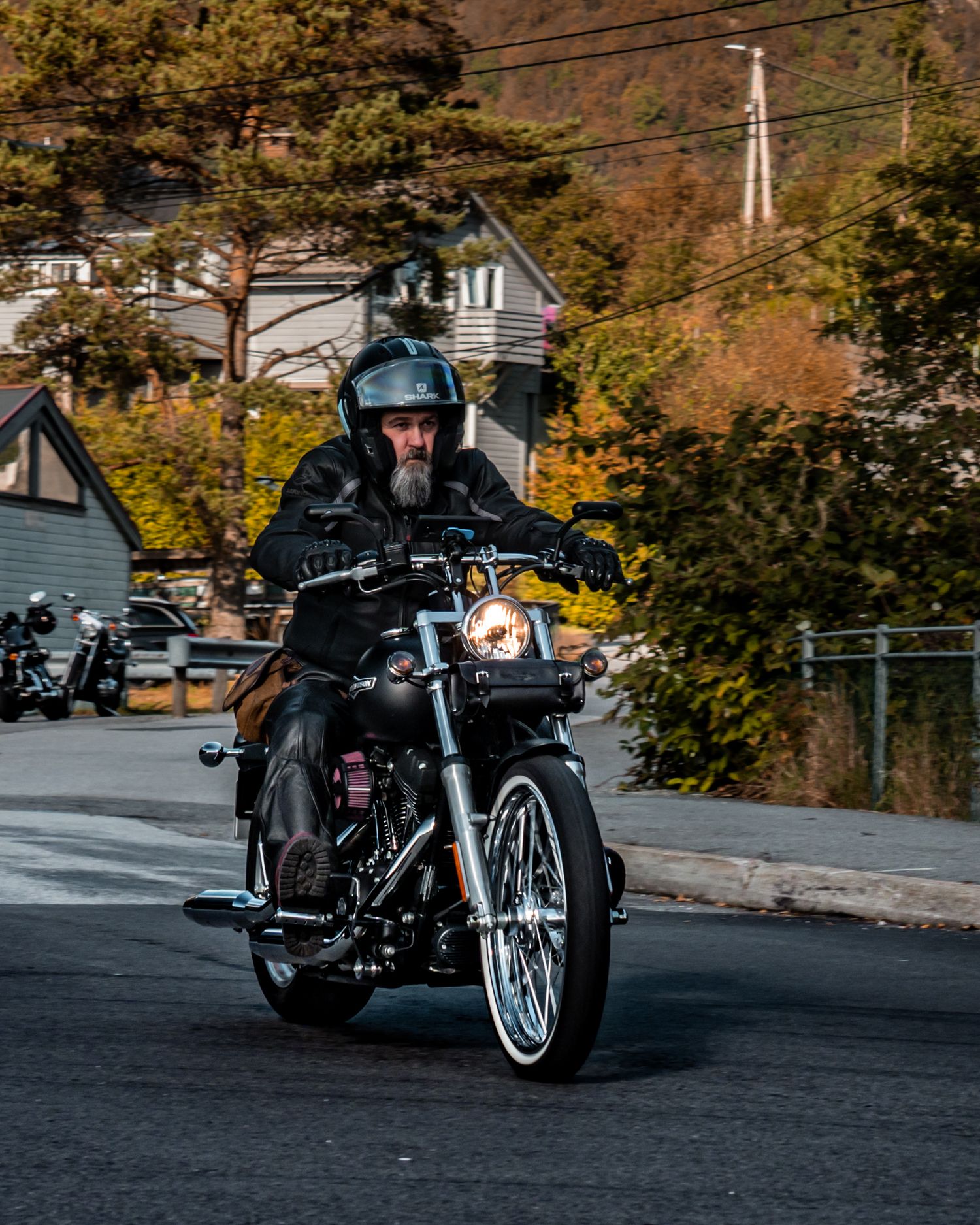 Classic motorcycle rider cruising through fall foliage on residential street.