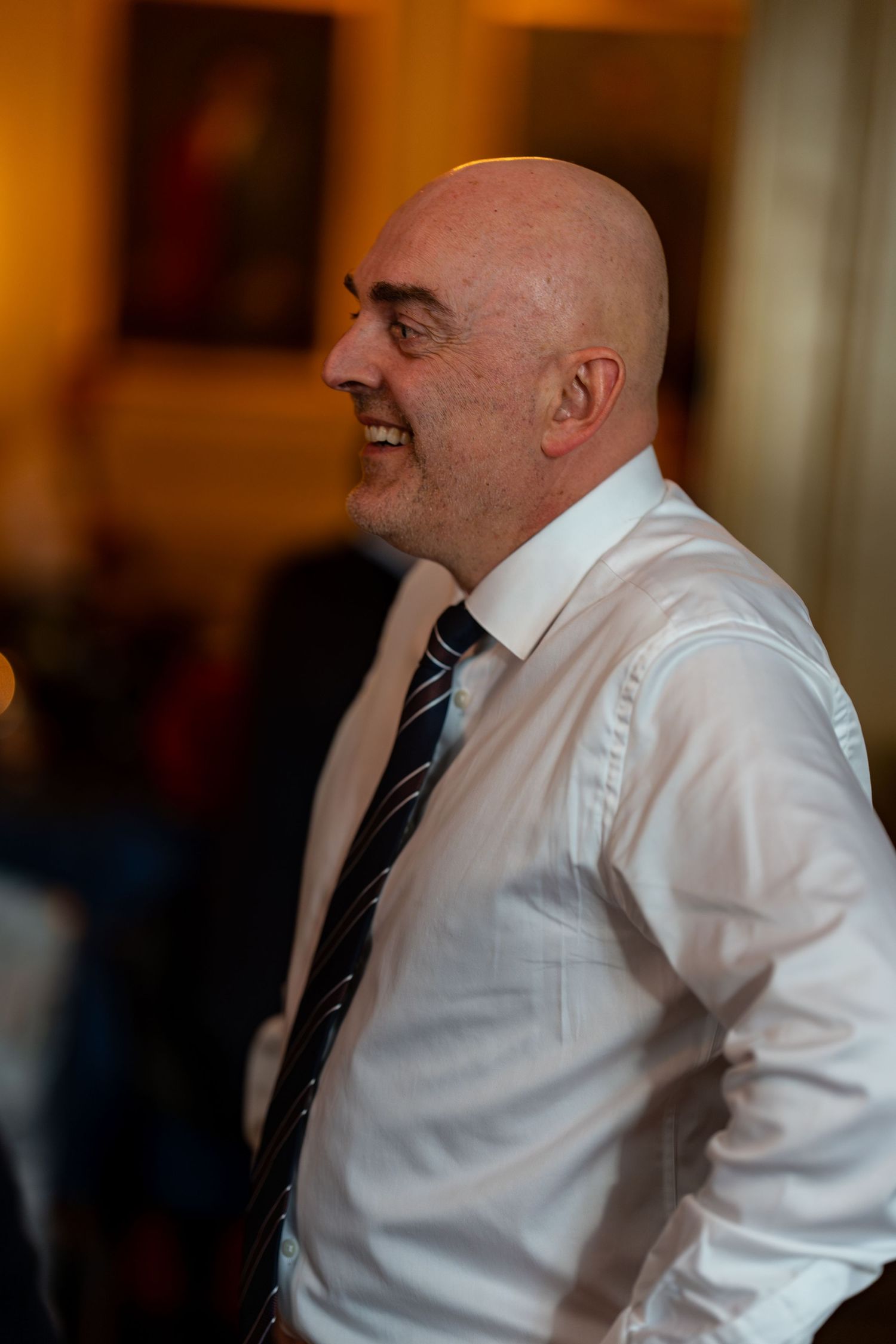 A guest in a white dress shirt and tie smiles warmly during an evening celebration.