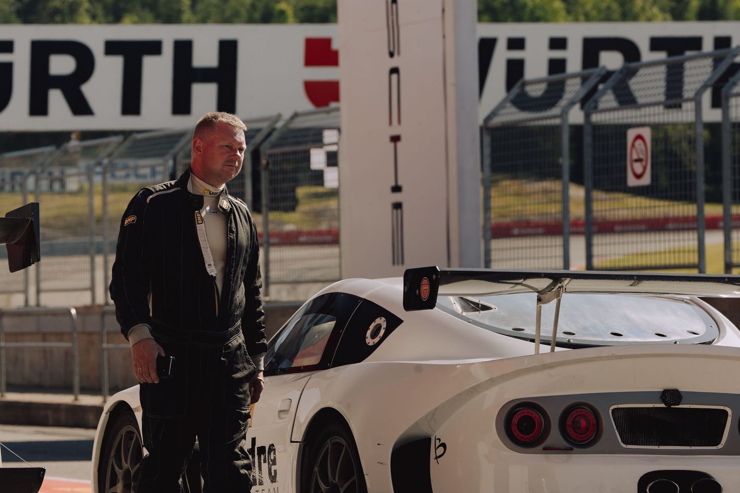 A white sports car is parked at a racing facility with someone standing beside it.