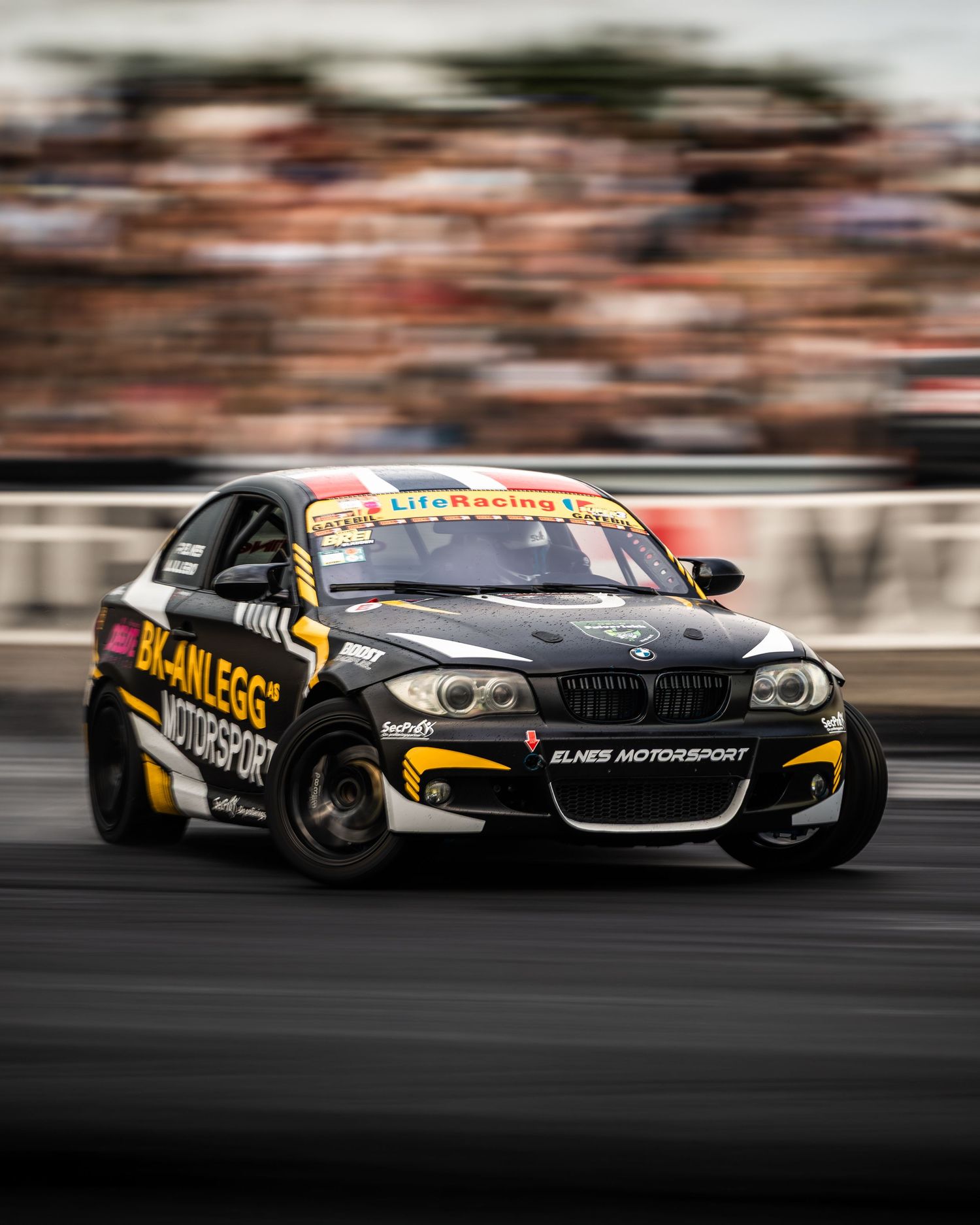 Motion-blurred BMW race car with black and yellow livery speeding on a racetrack during competition.