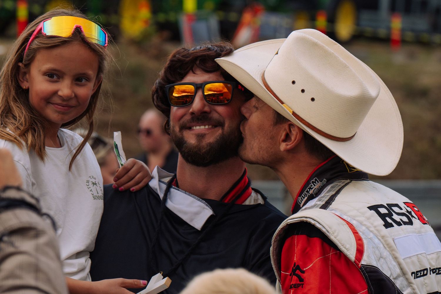 Spectators gather outdoors at a casual event wearing cowboy hats and sunglasses while enjoying themselves.