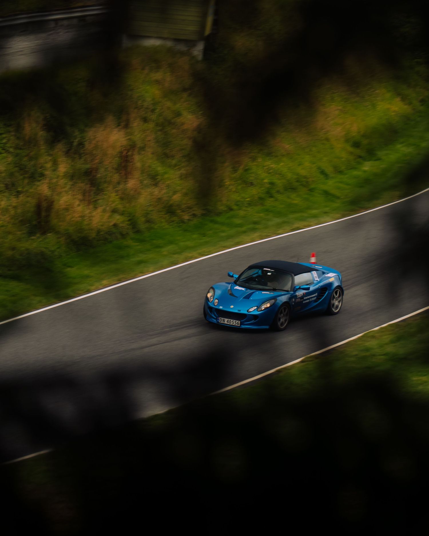 Aerial view of a blue McLaren sports car driving on a winding road surrounded by lush green foliage.