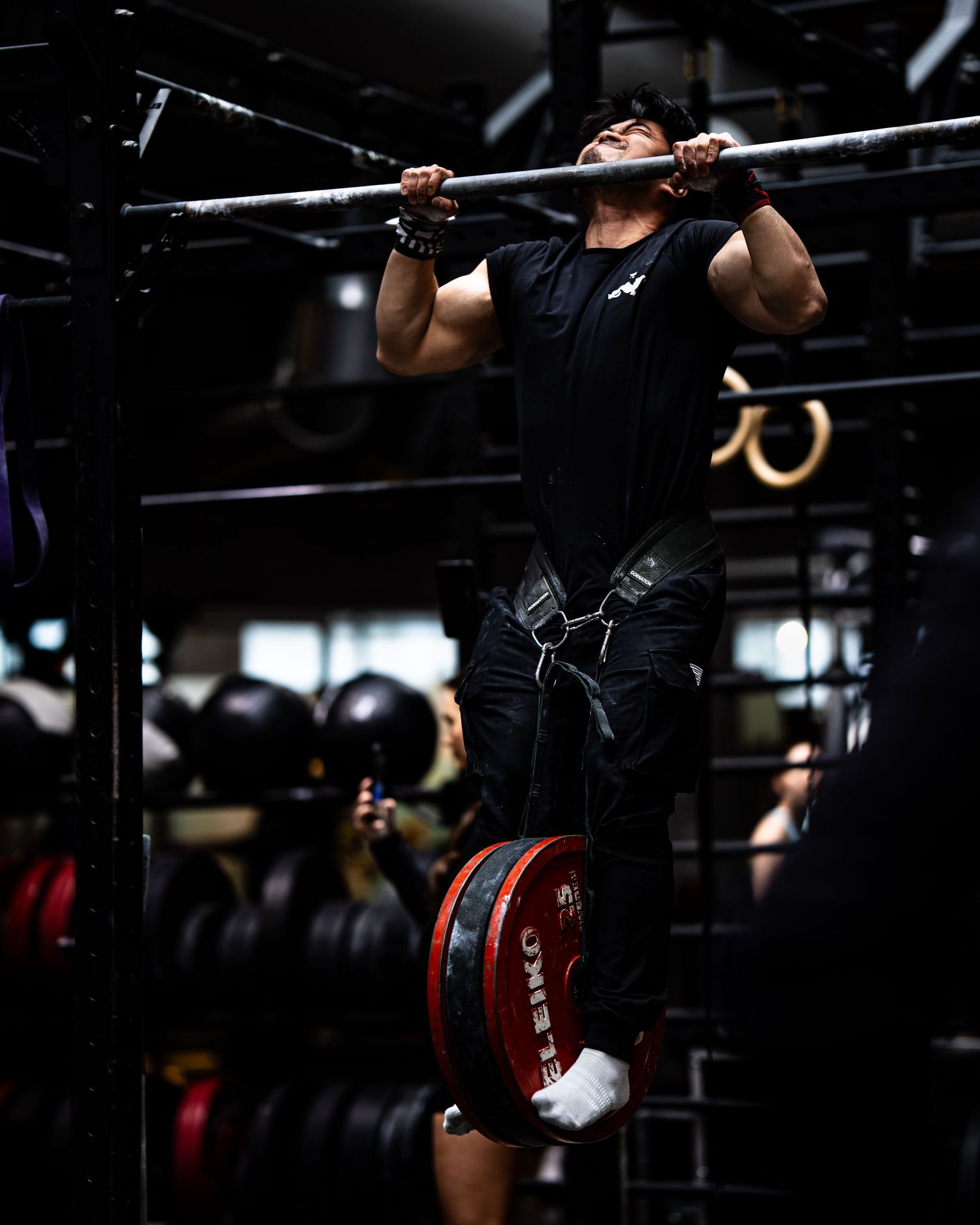 Athlete executes weighted pull-up with proper form in dark gym environment.