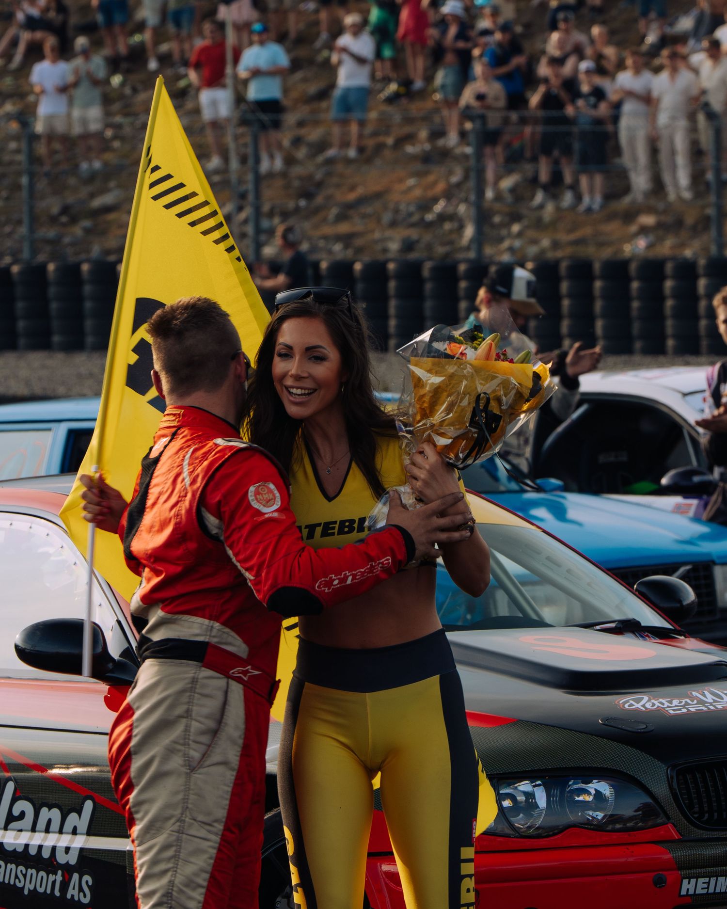 Racing event scene with yellow flag and motorsport vehicles in the background.