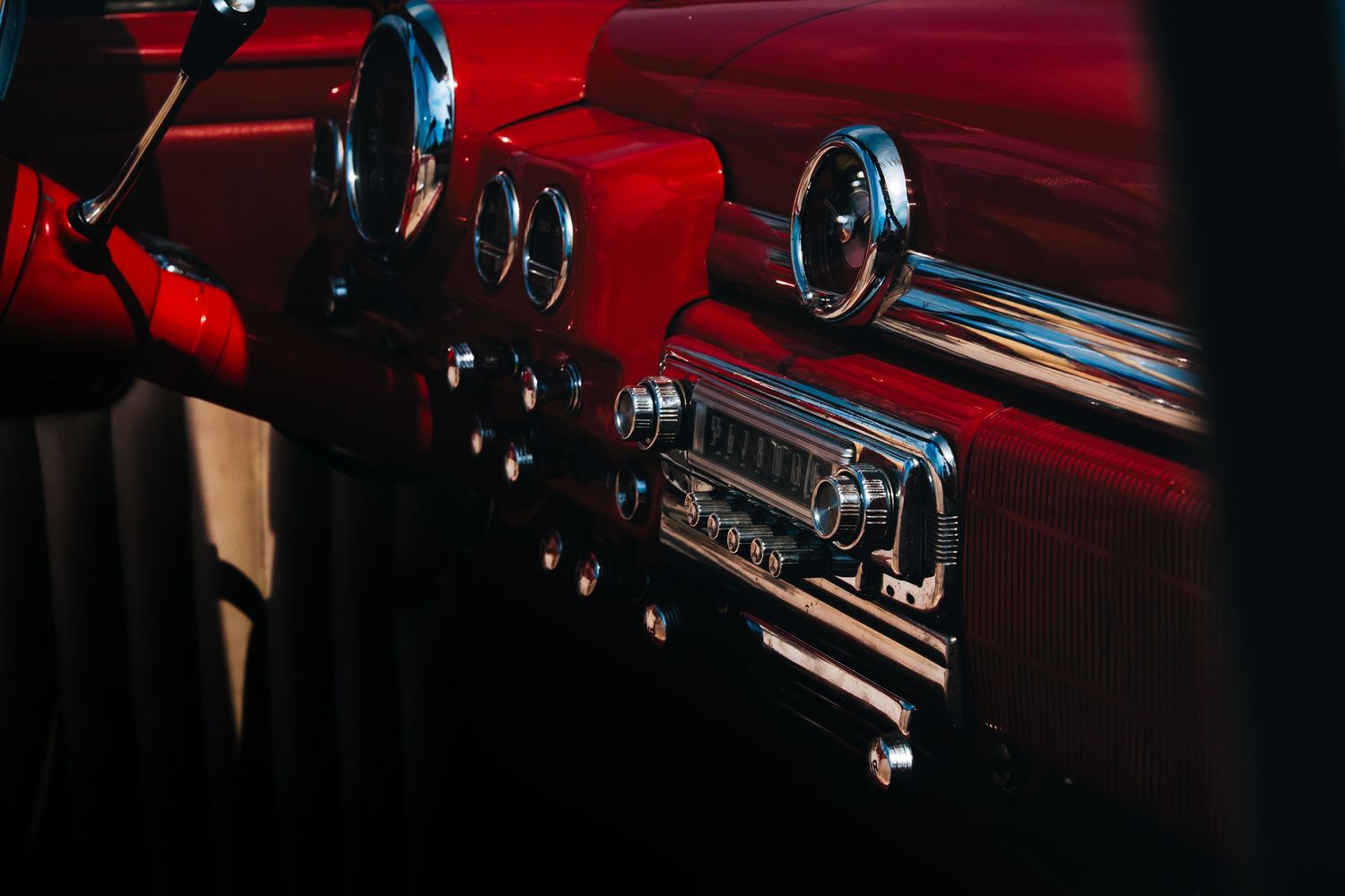Interior dashboard details of a classic car illuminated in dramatic red lighting.