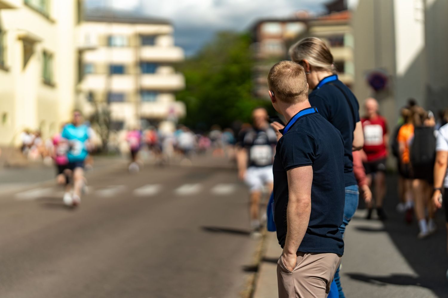 People walking outdoors on a sunny day with urban buildings visible in the background.