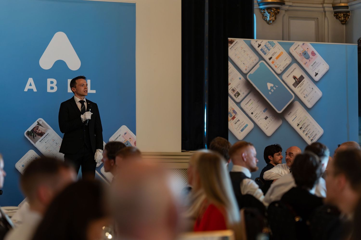Corporate event space with ABEL branding visible on blue backdrop and attendees mingling.