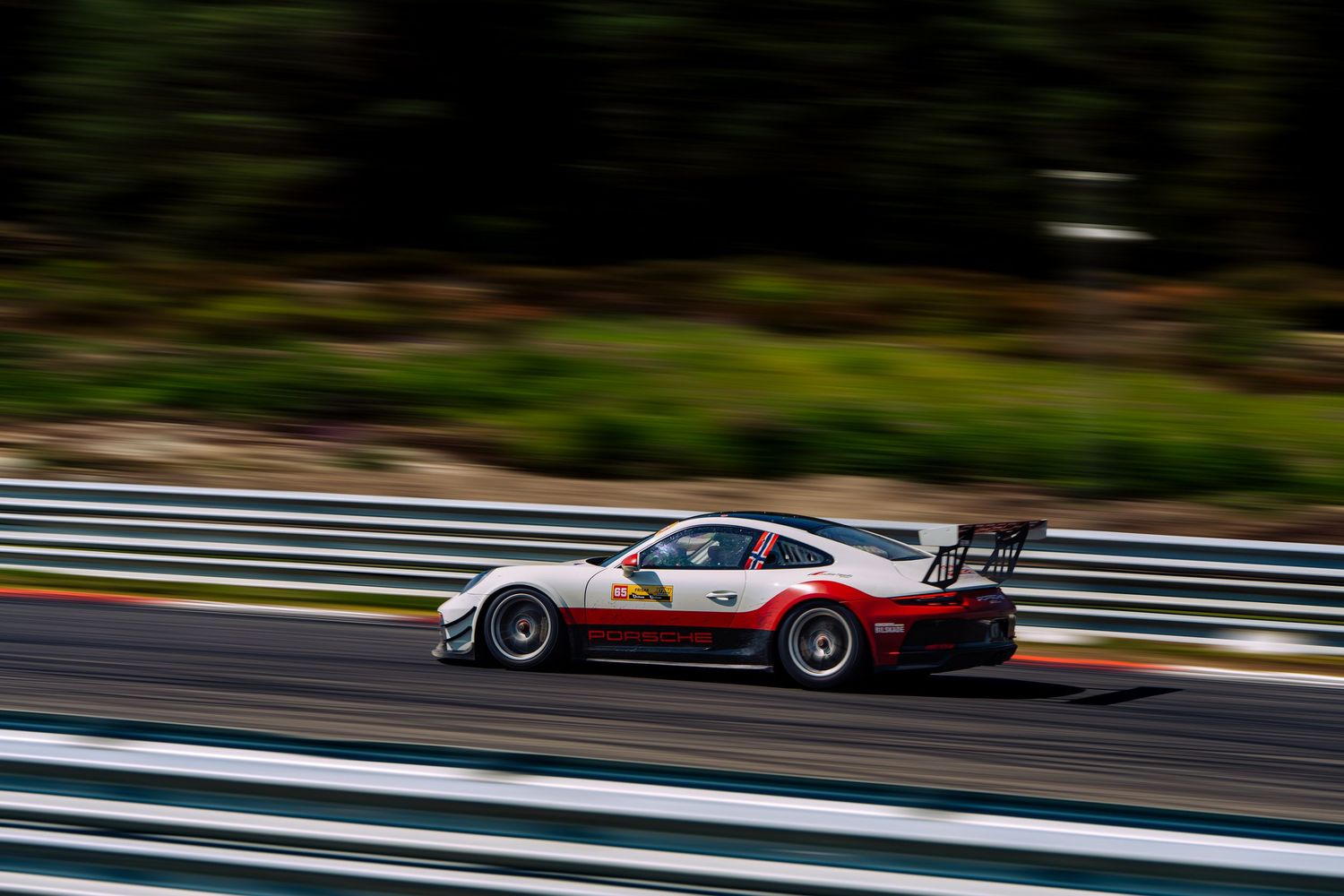A red and white race car speeds around a racetrack with motion blur effect in the background.