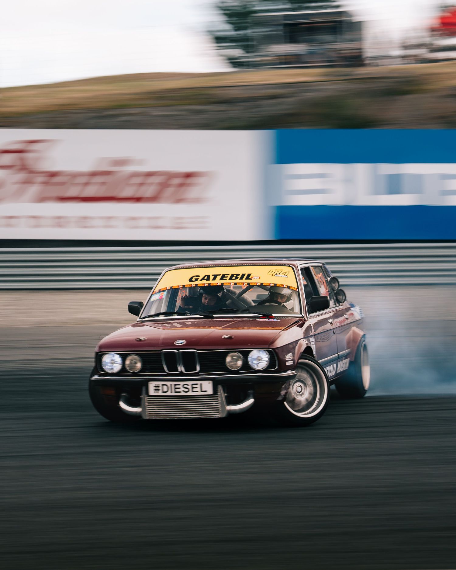 A brown BMW sports car drifting on a race track with motion blur, creating a dynamic action shot.