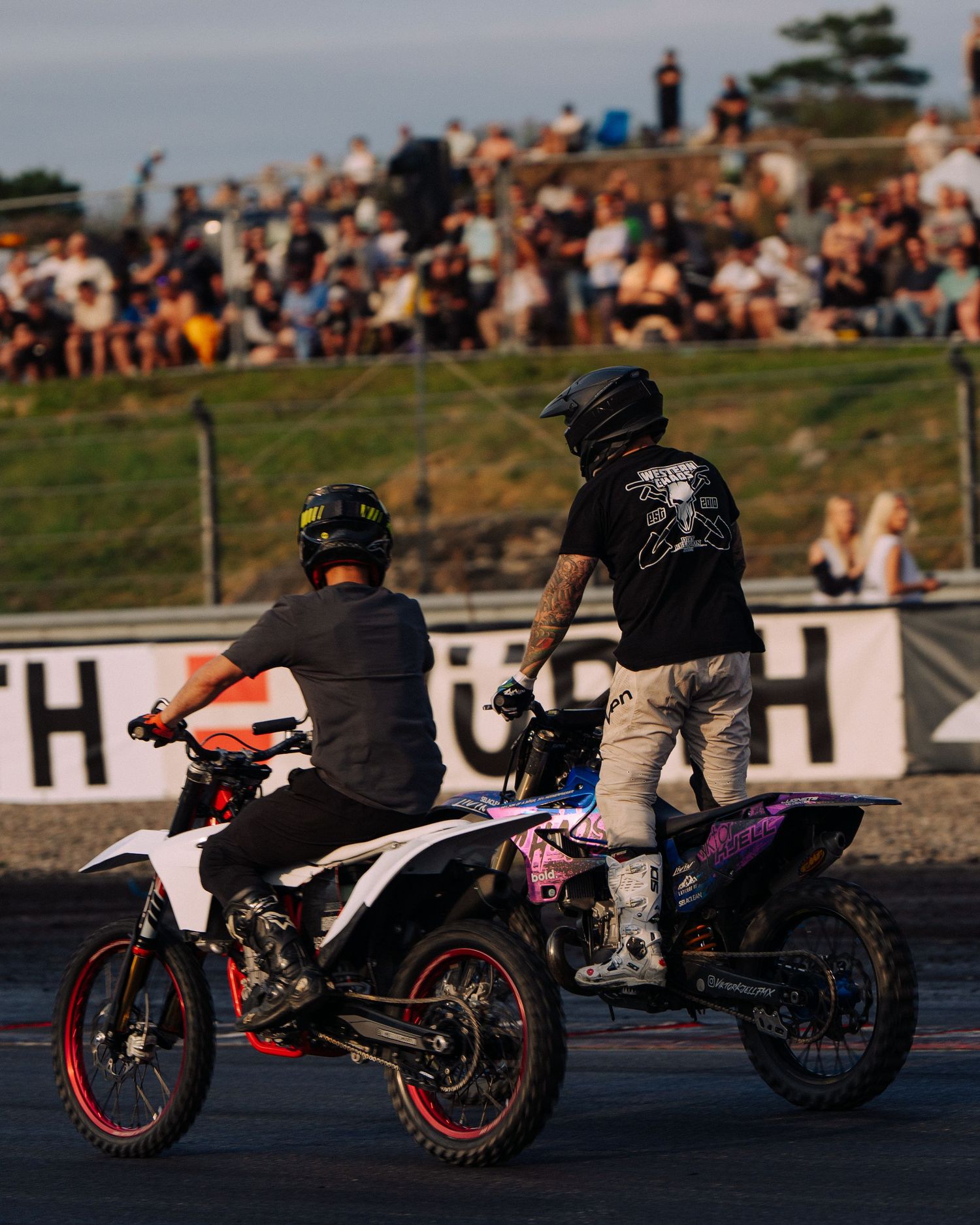 Silhouetted motorcyclists performing stunts on recumbent bikes at sunset by the waterfront.
