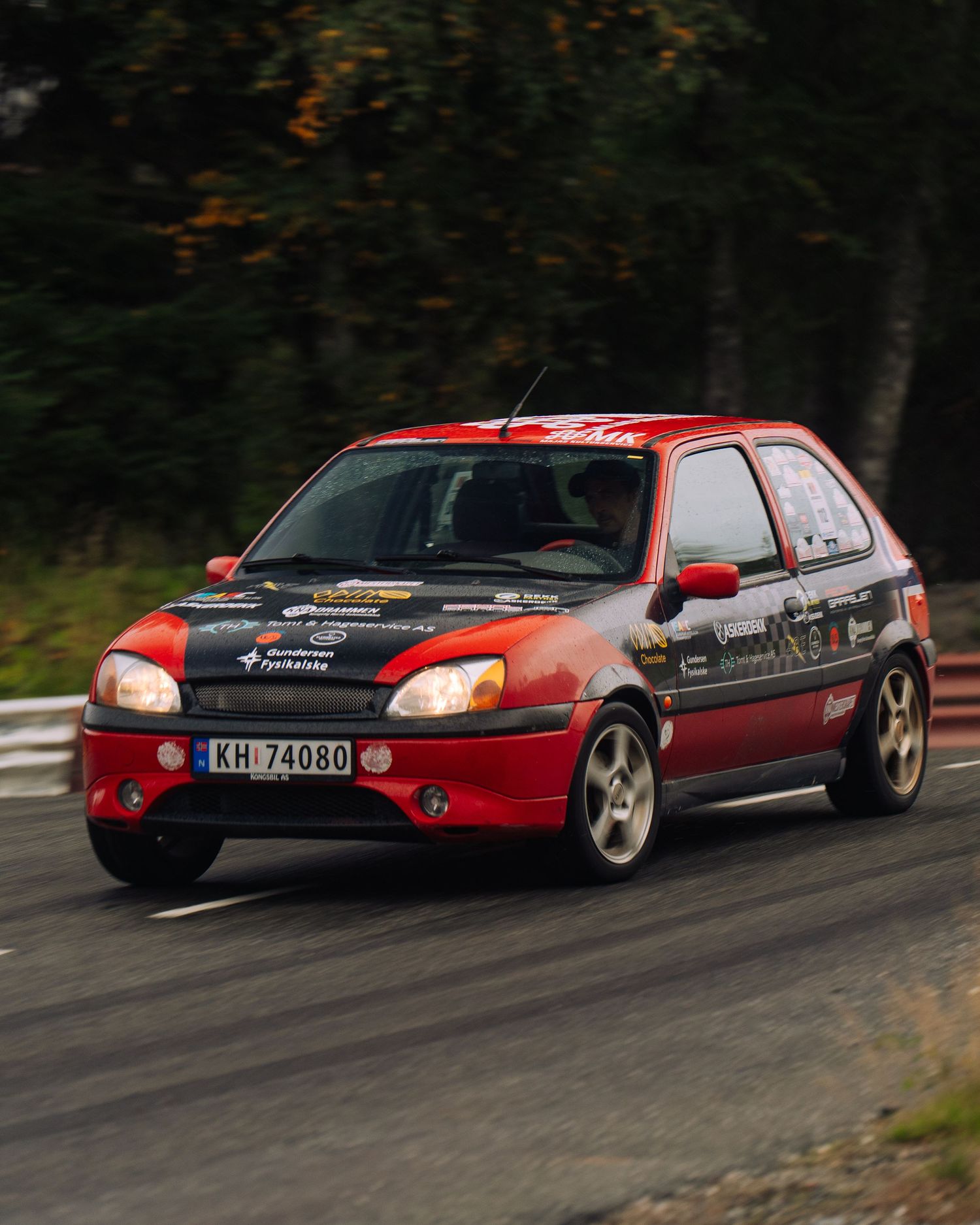 A red sports car drifts around a curve on a dark forest road during an intense racing moment.